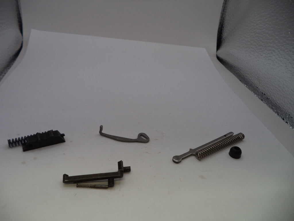 Four small metal and black mechanical parts arranged on a white sheet, photographed against a light gray textured backdrop.