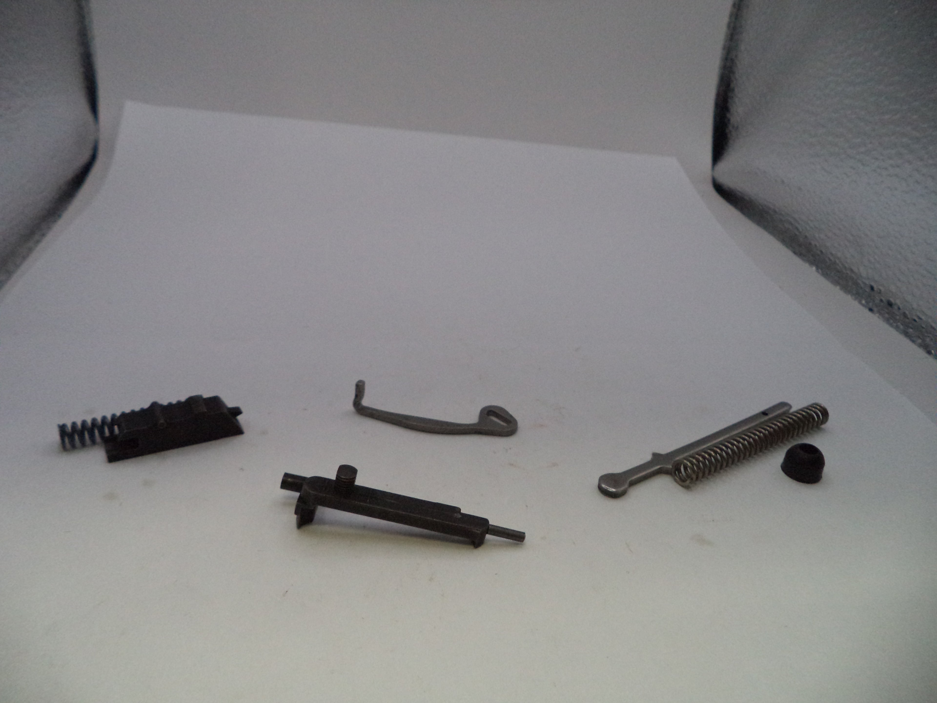 A set of small metal and black mechanical parts, including springs, rods, and a curved hook, arranged on a white surface.