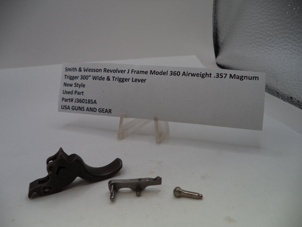 A used Smith & Wesson revolver J frame trigger lever set for a .357 Magnum, including the black trigger lever, a silver metal piece, a small screw, and a white product information card on a clear stand.