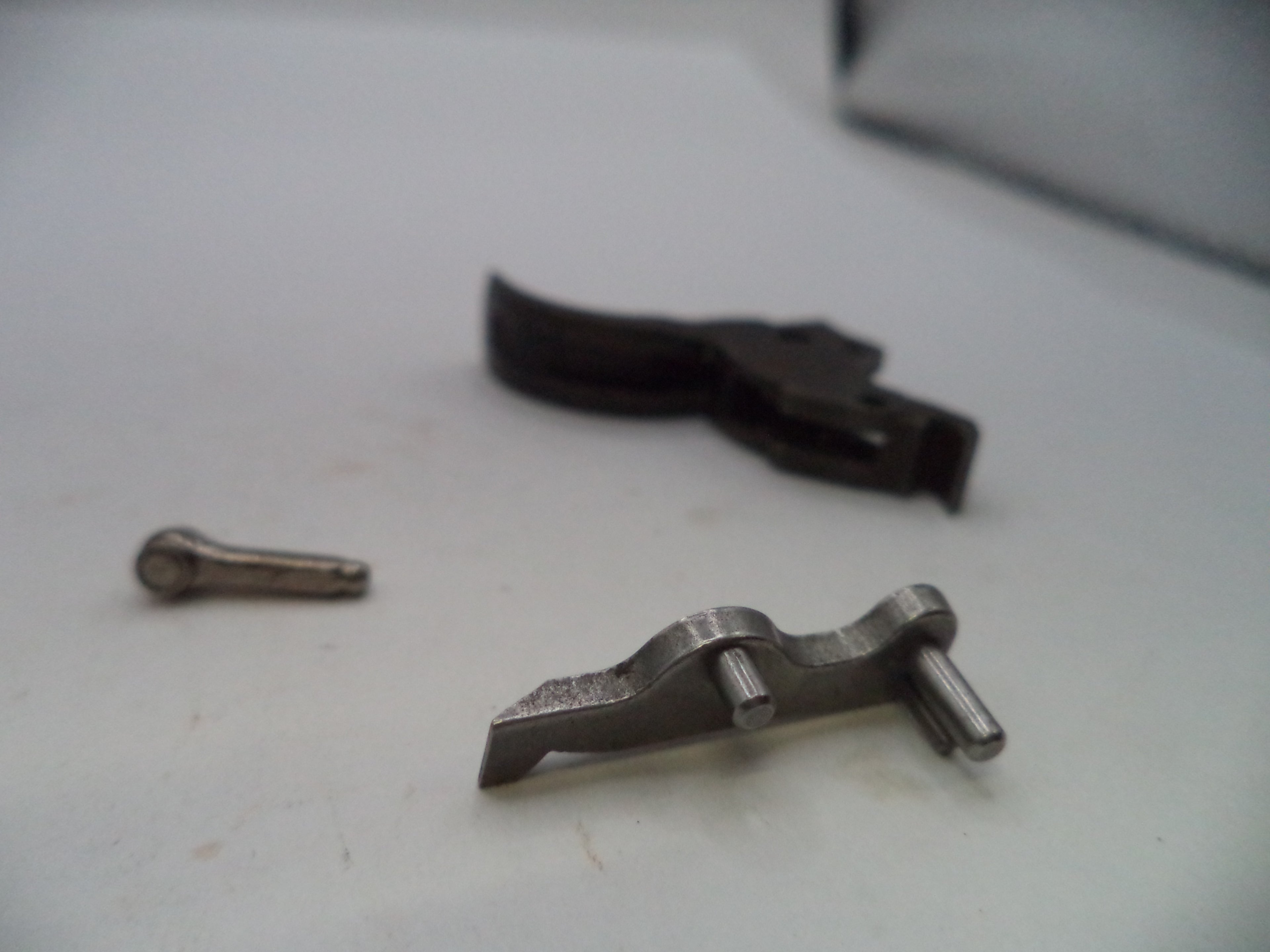 A set of small metal mechanical parts, including a silver-toned lever and a dark metal piece, resting on a light-colored surface.