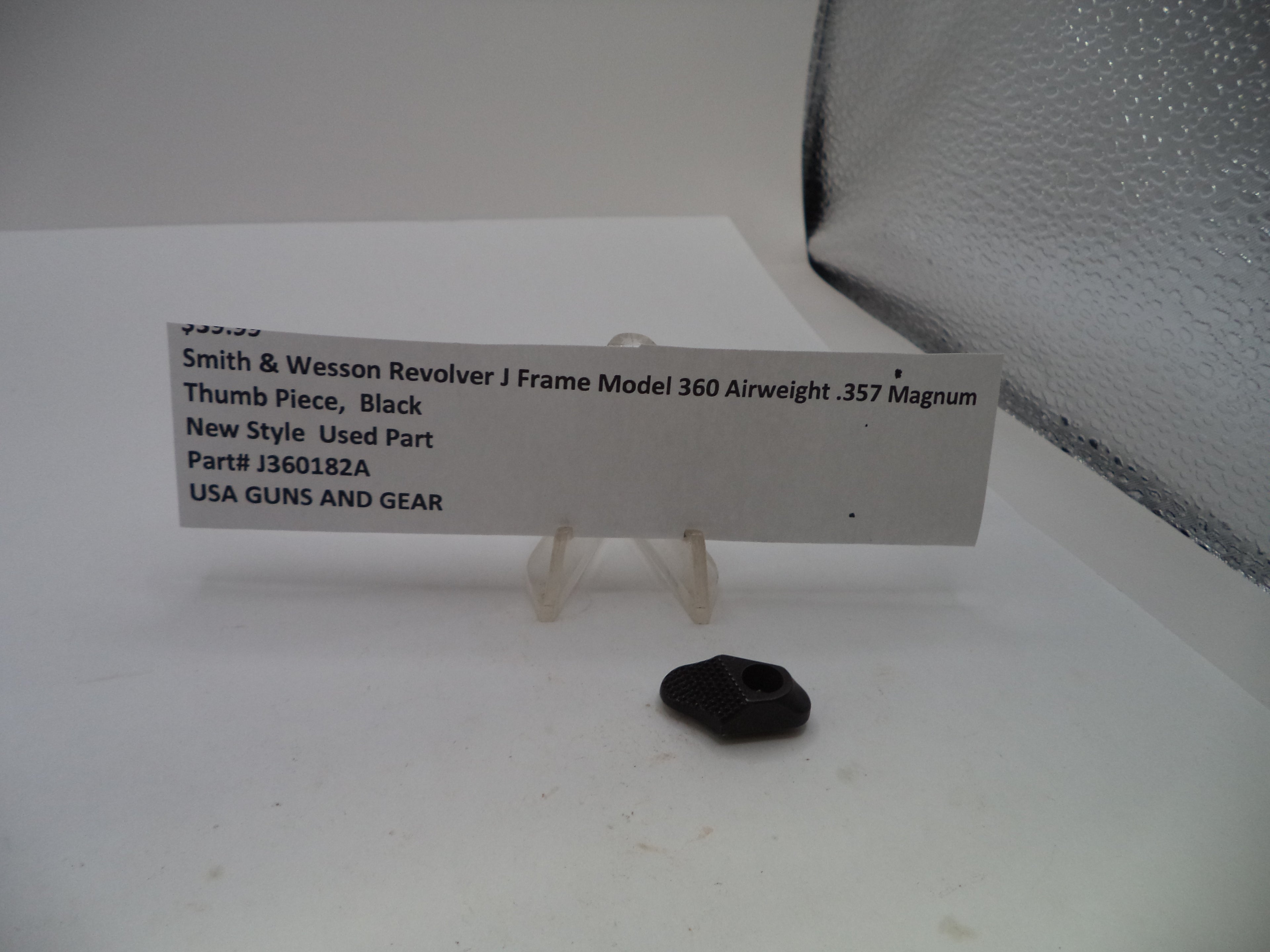 A small black thumb piece for a Smith & Wesson Revolver J Frame Model 360 airweight .357 Magnum handgun, displayed on a clear stand next to a white paper label with product details.