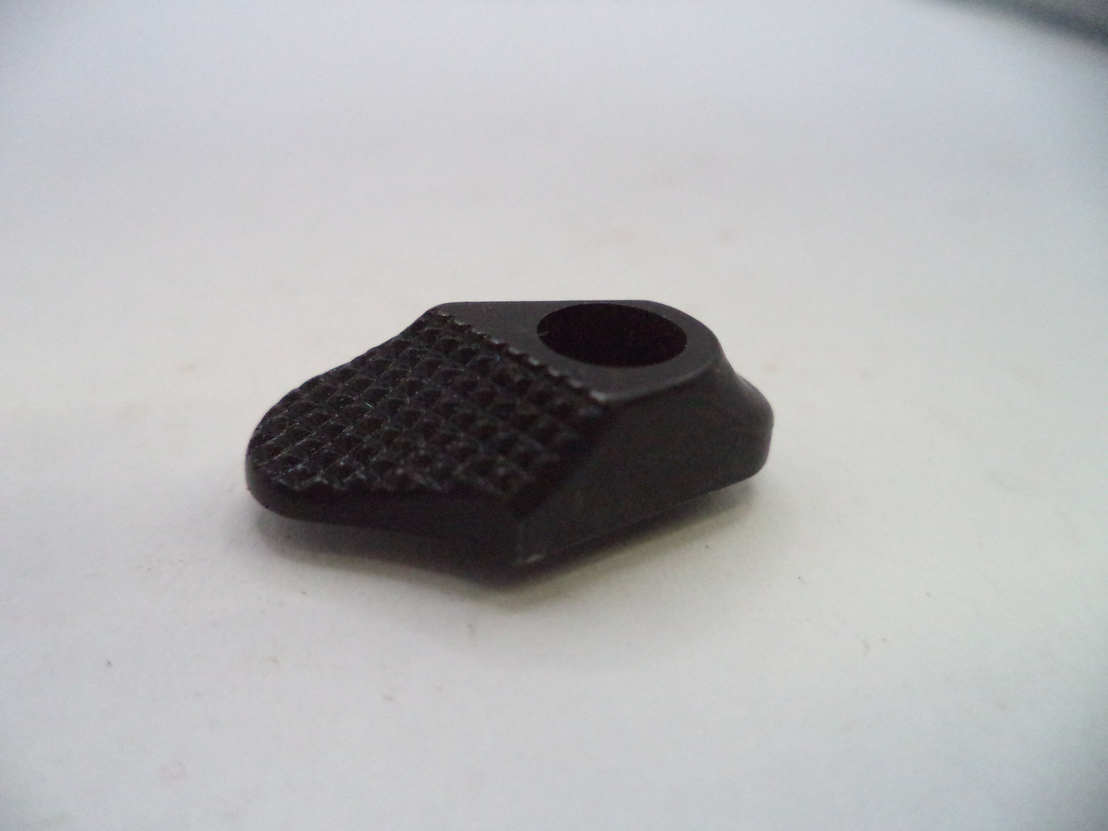 A small black plastic or rubber component with a textured grip surface and a circular hole, photographed on a plain light background.