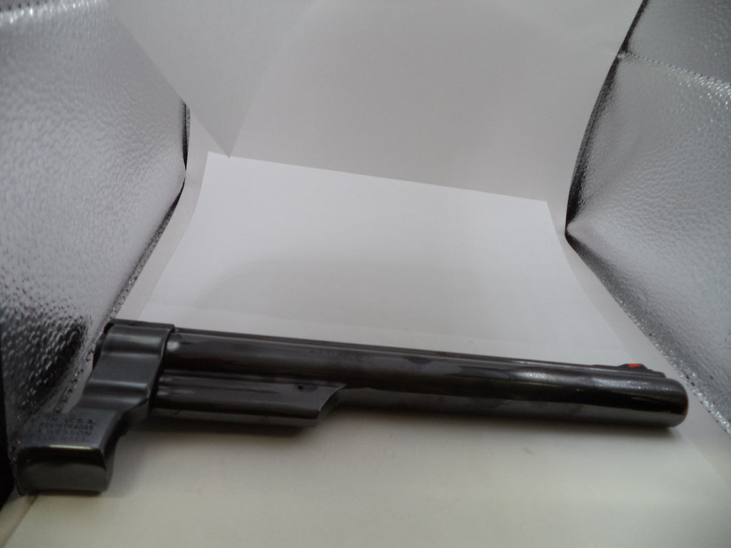 A black metal revolver-style object photographed inside a lightbox with reflective silver walls and a white center panel.