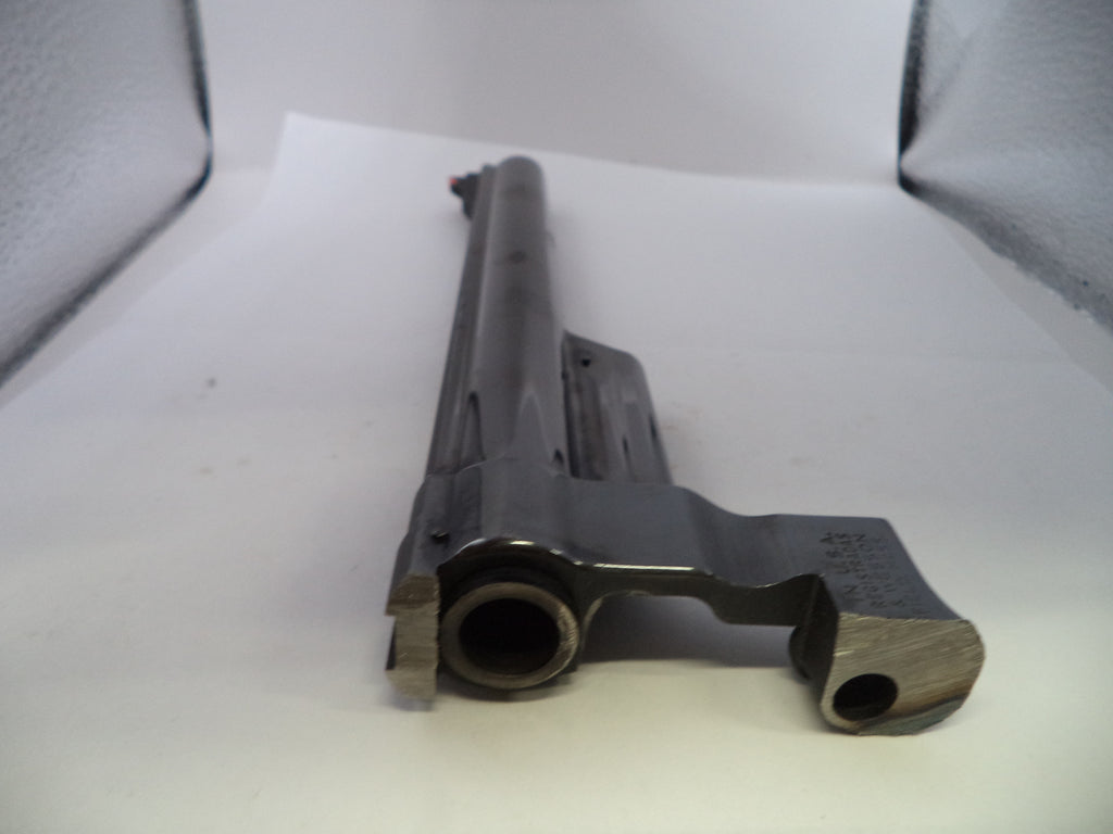 A close-up of a dark metallic gun receiver and barrel section photographed on a white surface with a textured gray backdrop.
