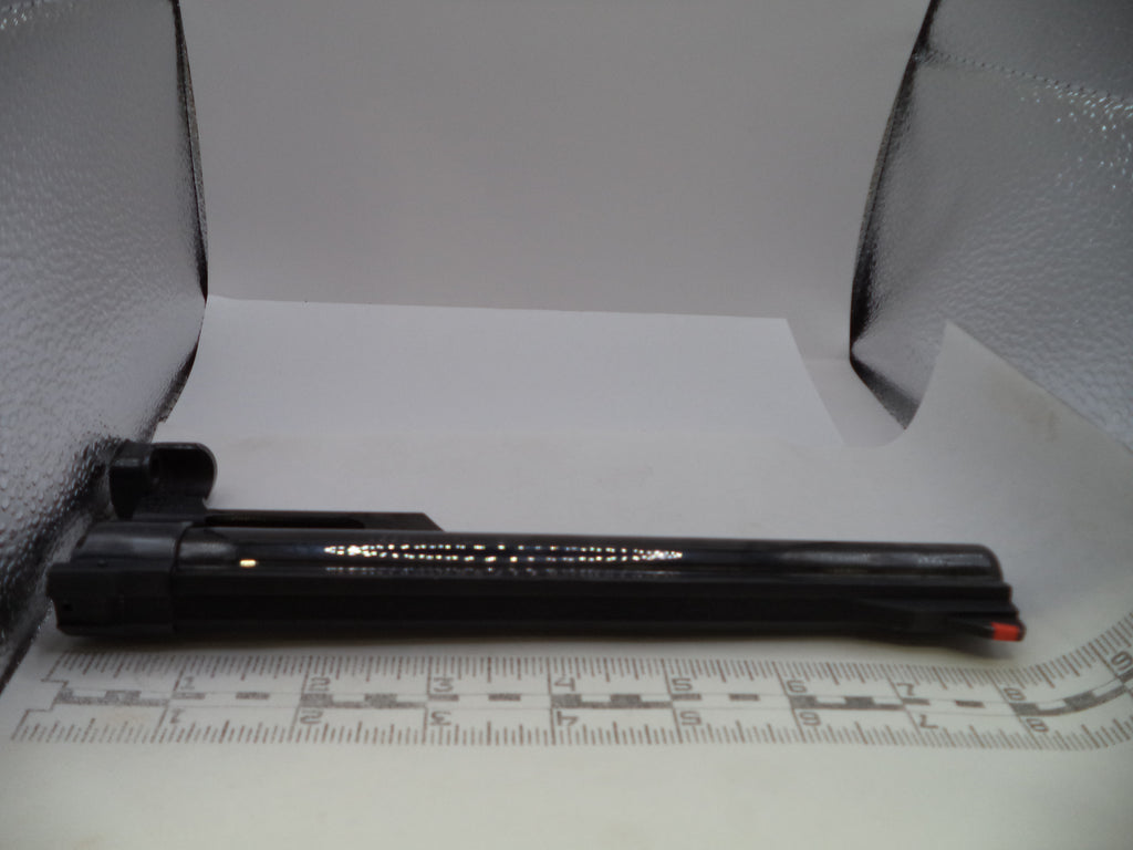 A black rifle scope mount or accessory bar with gold lettering, shown on a white background with a measuring ruler in front and textured silver walls behind.