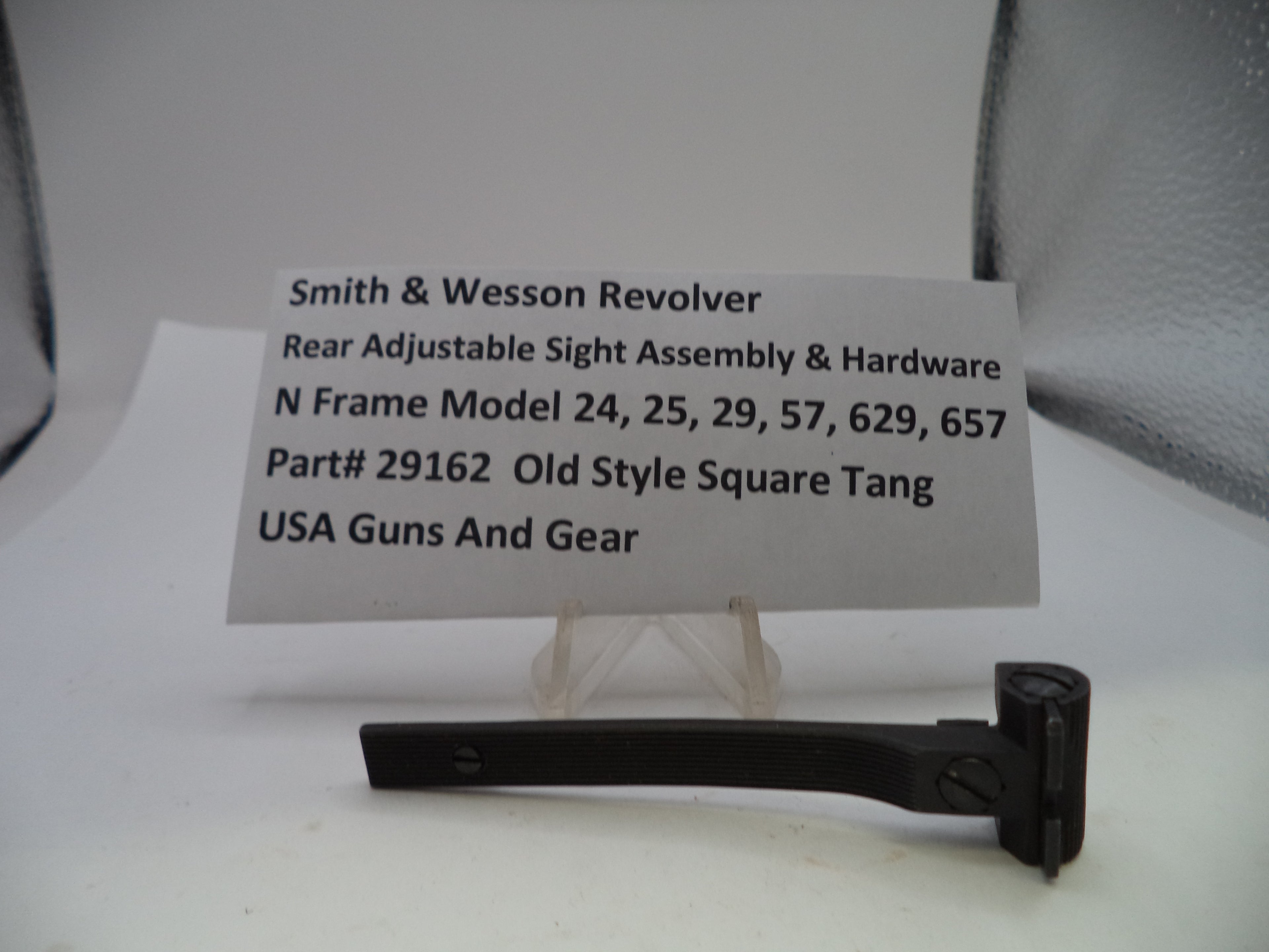 A black metal rear adjustable sight assembly hardware piece displayed on a small clear stand, with a white label card behind it reading 'Smith & Wesson Revolver Rear Adjustable Sight Assembly & Hardware' and part number 29162.