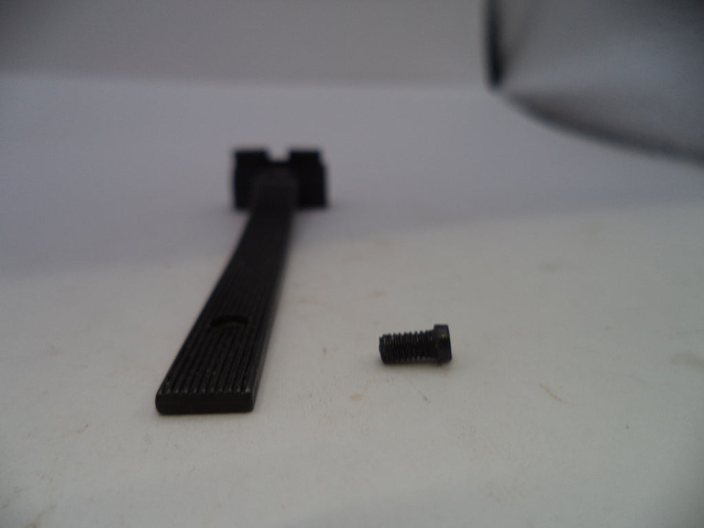 A black metal mounting bar with a ribbed textured surface and a small black screw placed beside it on a light gray surface.
