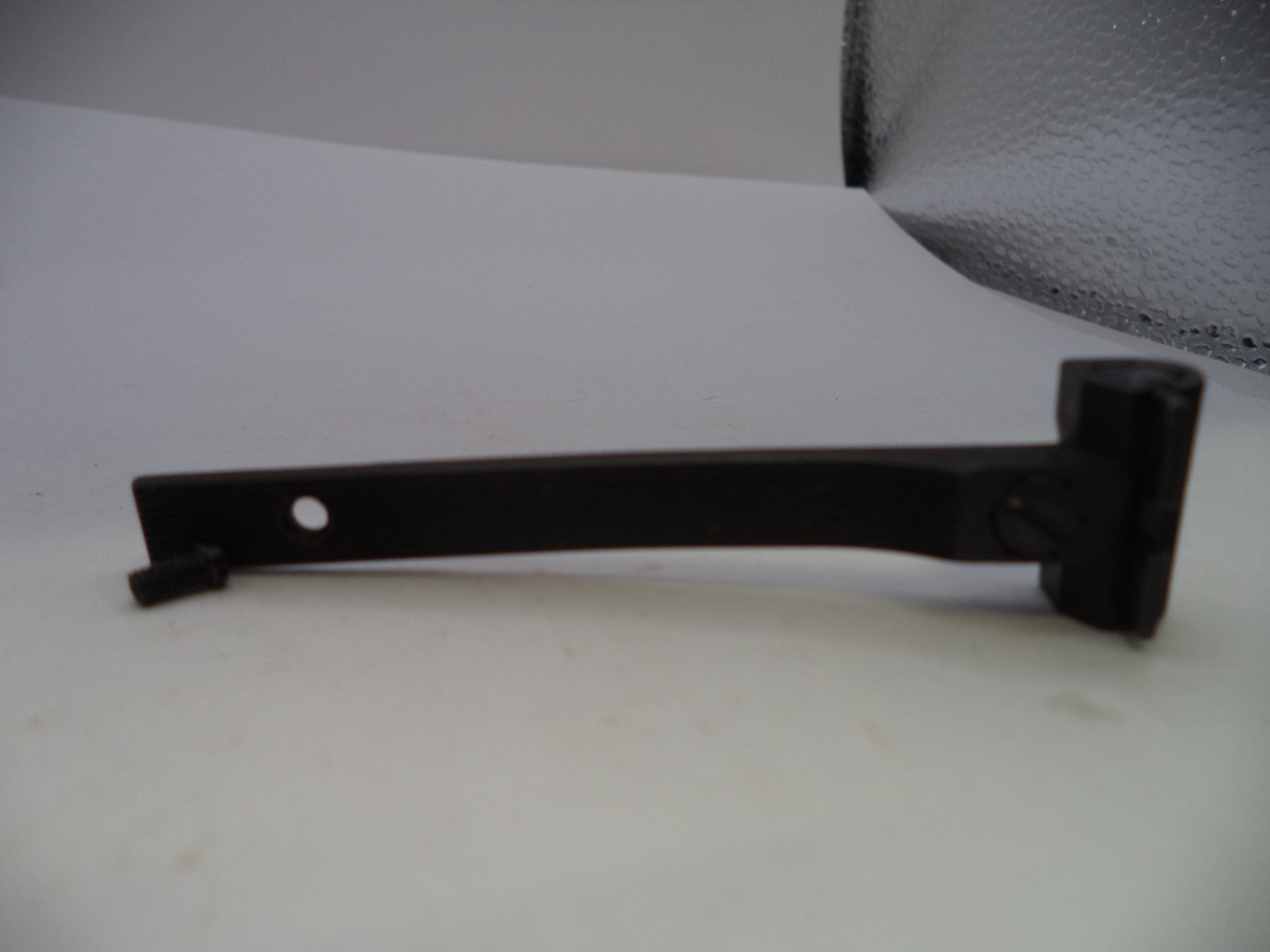 A black metal door stopper or latch arm with a mounting hole, shown on a white surface.
