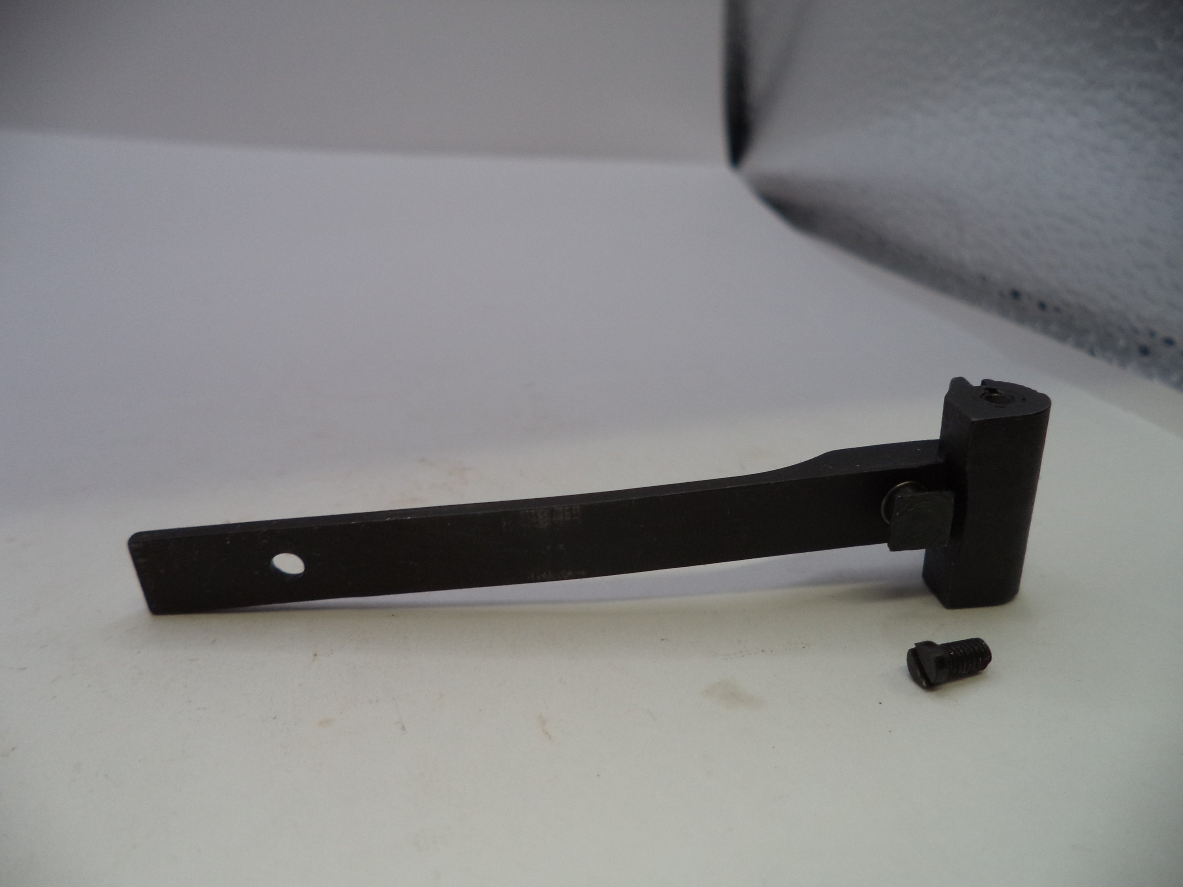 A black metal latch or bracket with a small mounting screw placed beside it, photographed on a light gray surface.