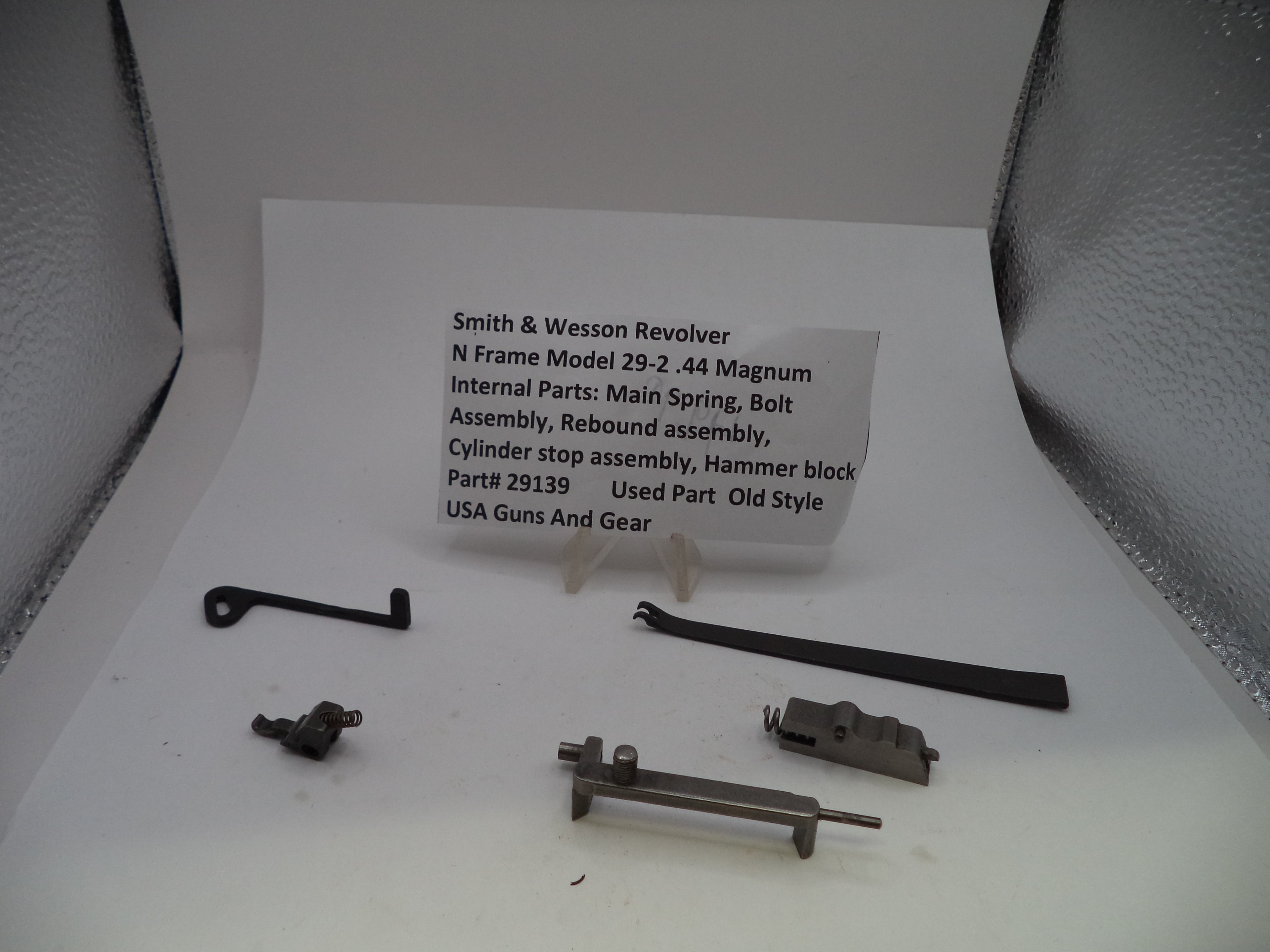 Internal parts of a Smith & Wesson Revolver N Frame Model 29-2 .44 Magnum, including a main spring, bolt, rebound assembly, cylinder stop assembly, and hammer block, displayed on a white surface with a product information card.