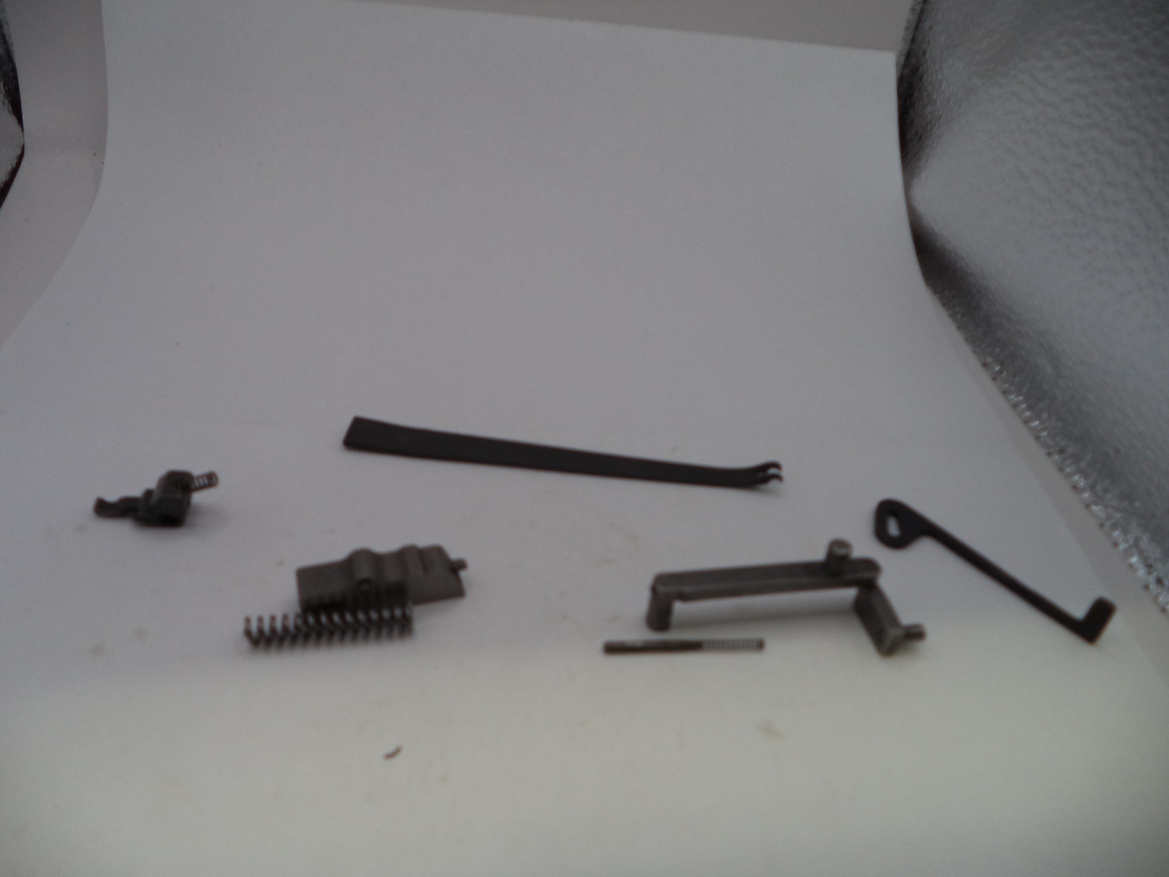 A set of small dark metal mechanical parts and springs arranged on a plain white surface.