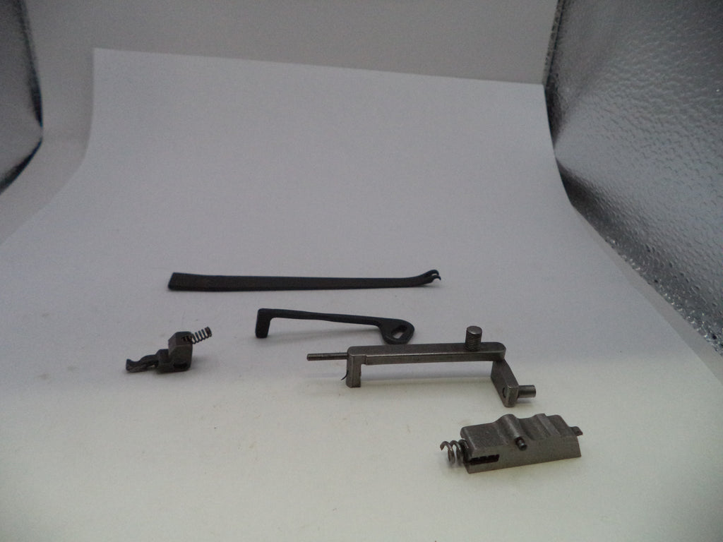 A set of small metal and black hardware components, including a long black strip, a dark metal bracket, a small black spring piece, and a gray metal latch or clip, arranged on a white studio background.