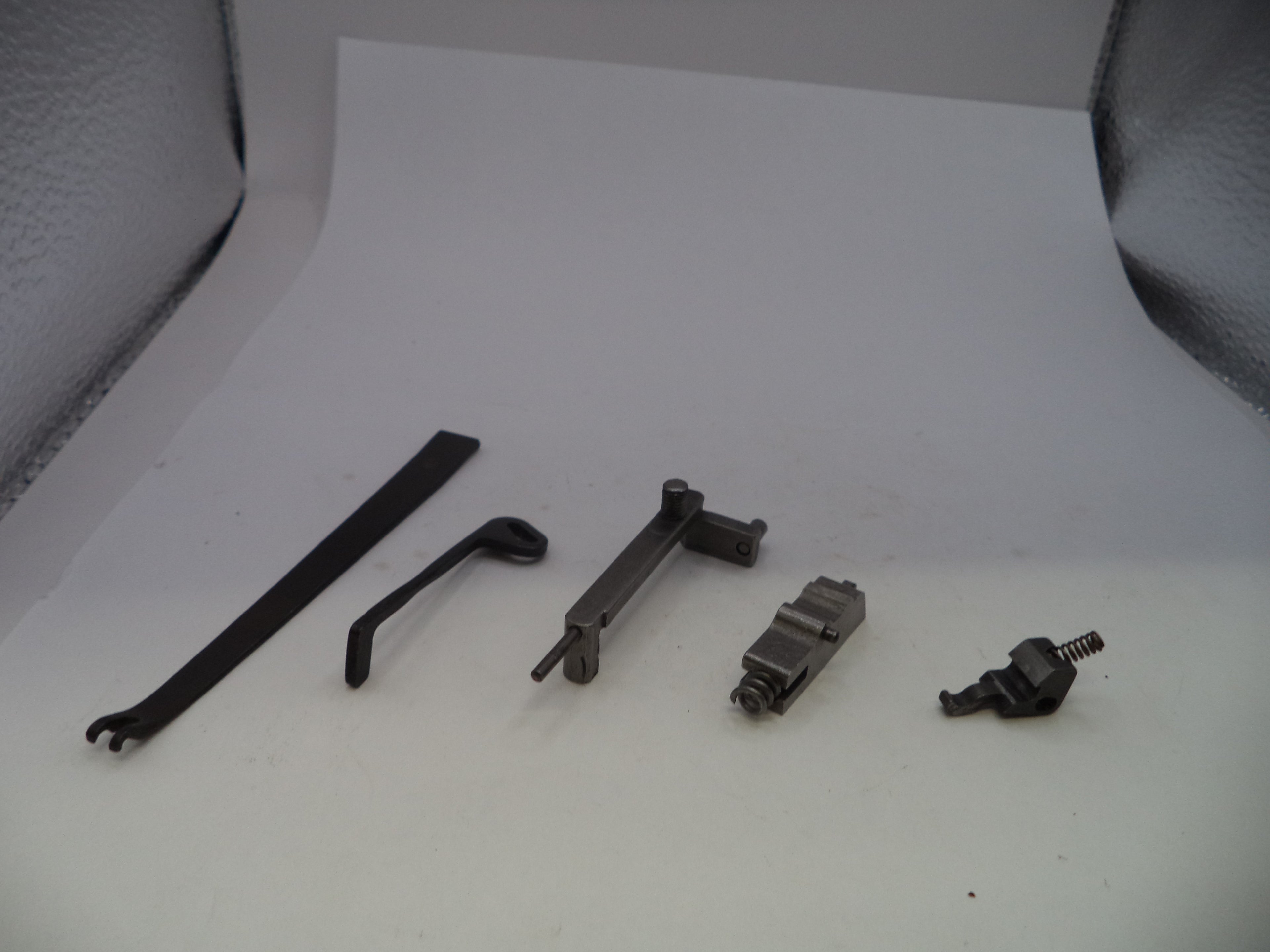 A set of five small black and dark gray metal mechanical parts arranged in a row on a white surface, photographed against a white backdrop with textured gray corners.