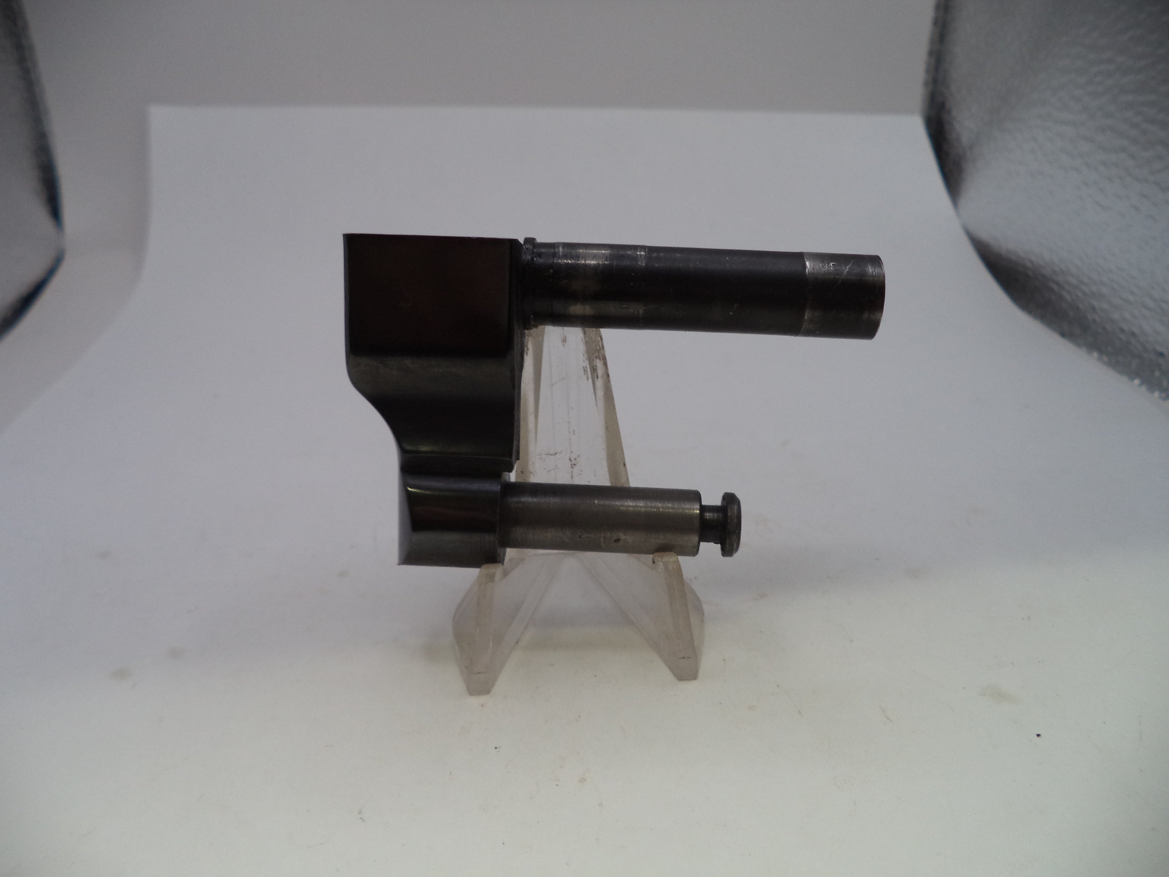 A dark metallic cylindrical tool or hardware piece mounted on a clear plastic display stand against a plain white background.