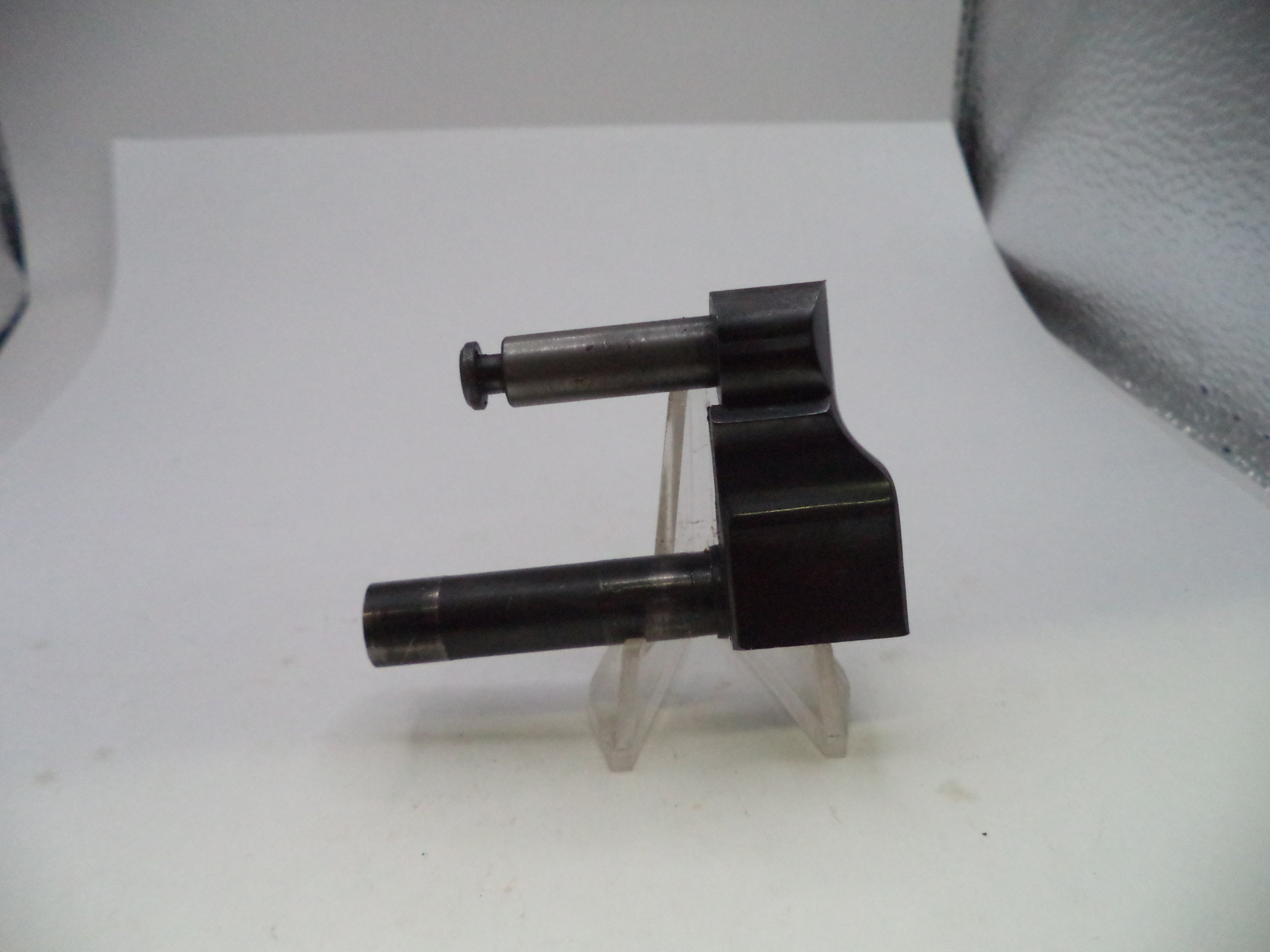A small black metal mechanical component with two cylindrical shafts, displayed on a clear plastic stand against a white background.