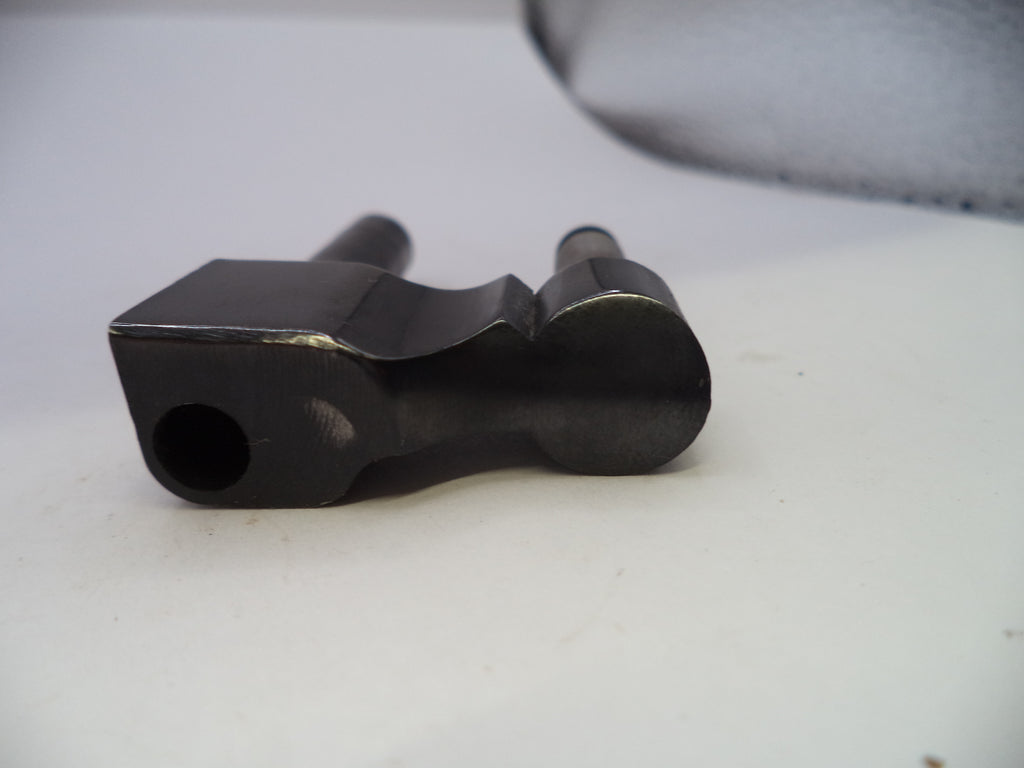 A close-up of a black metal machined part with a square opening and cylindrical shafts, resting on a white surface.