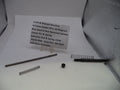 Smith & Wesson revolver replacement parts laid out on a white surface, including a long metal rod, two coiled springs, a small black cap, and a handwritten label card with part details.