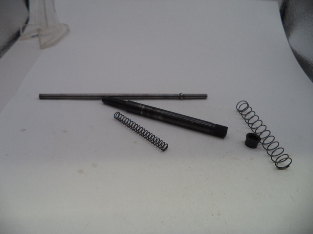 A set of metal mechanical parts, including a long rod, a black cylindrical component, two coiled springs, and a small black cap, arranged on a white surface.