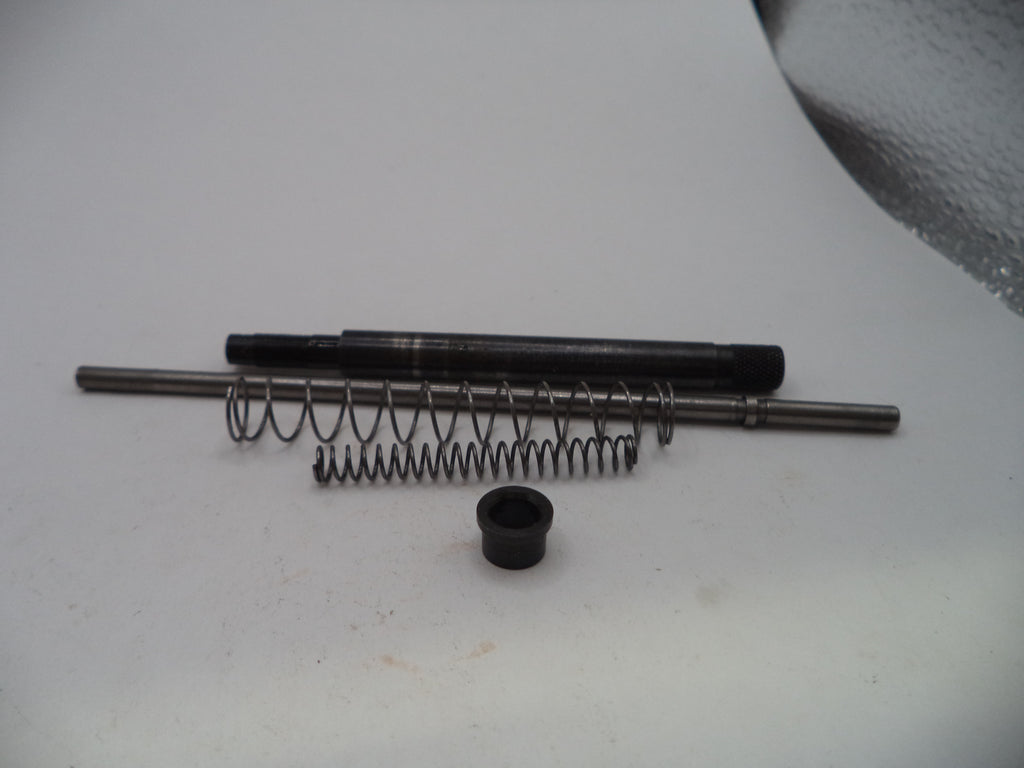 A set of small mechanical parts including a black metal rod, a coiled metal spring, a small black cylindrical piece, and a long silver metal rod, arranged on a white surface.