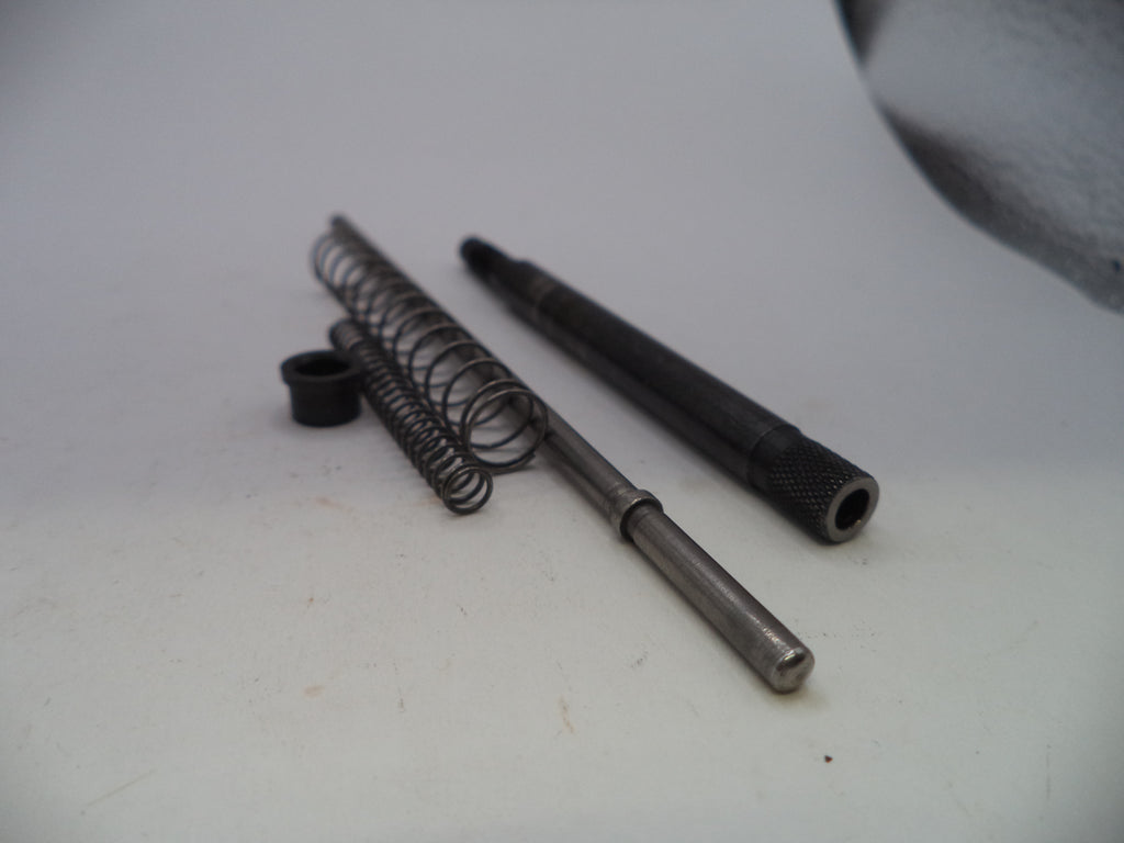 A set of small metal mechanical parts, including a coiled spring, a long metal rod, a black cylindrical component, and a small black ring, arranged on a plain light background.