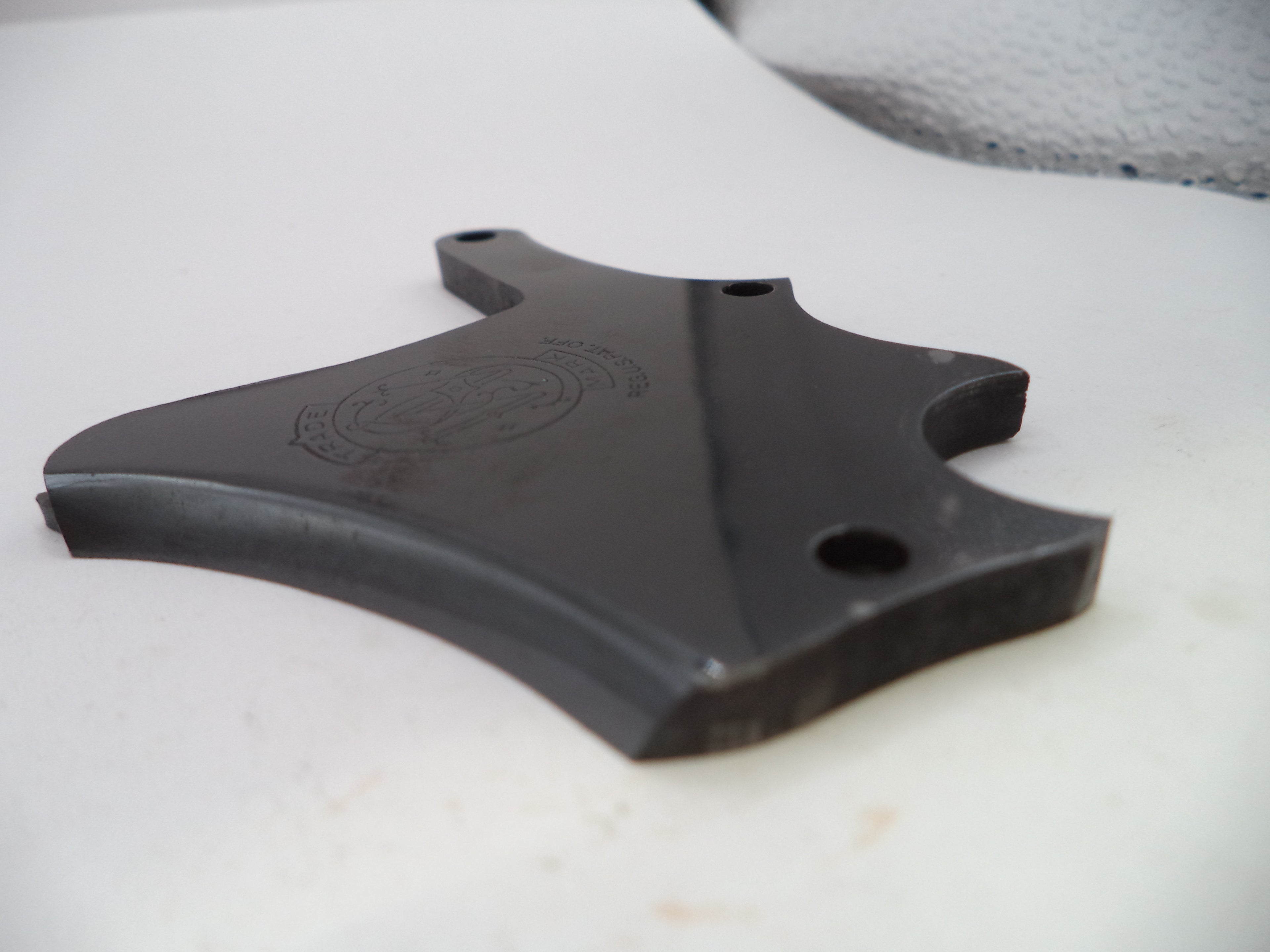 A black molded plastic replacement part with pre-drilled mounting holes, resting on a white surface.