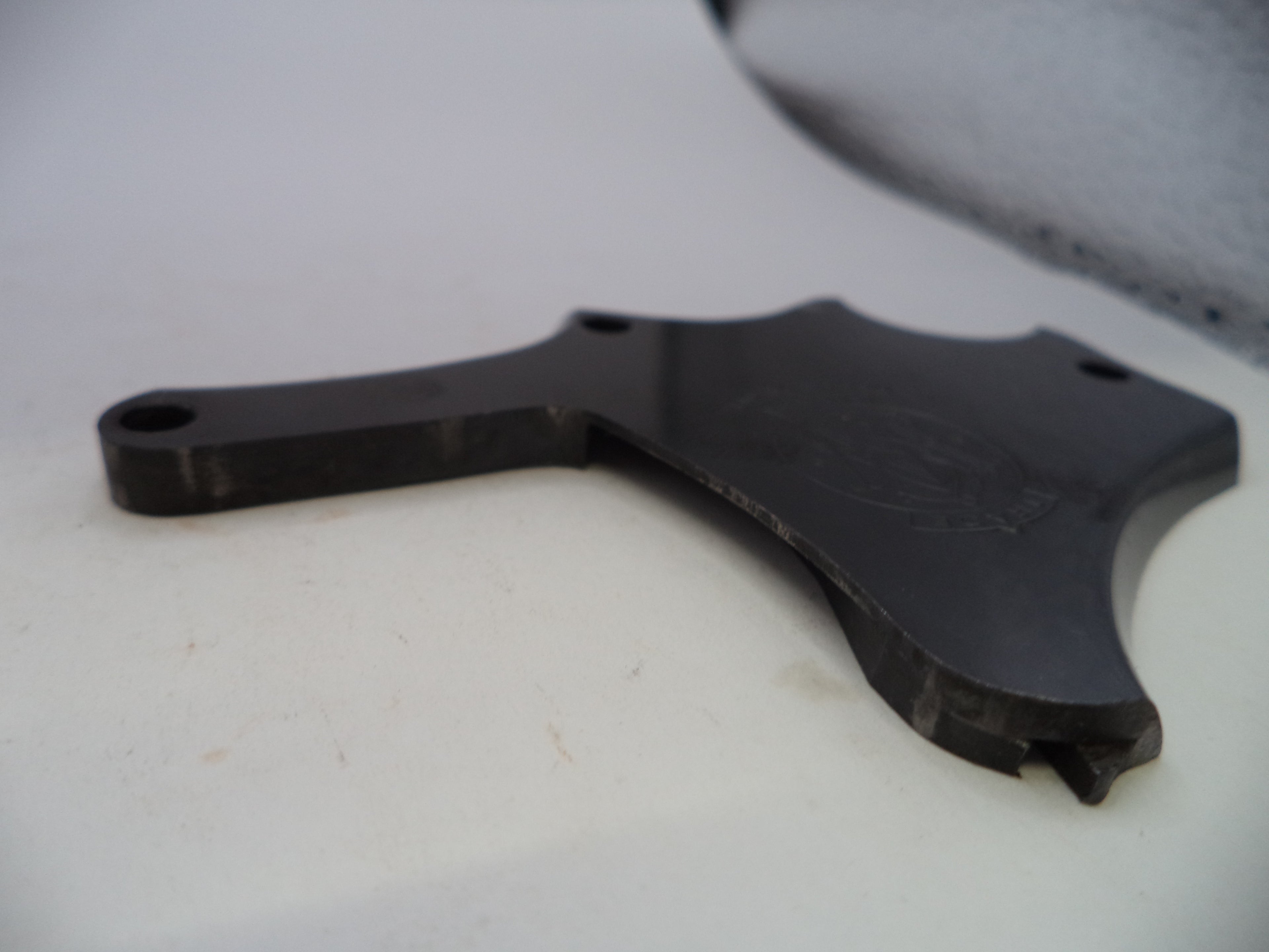 A black metal mounting bracket or hardware piece with pre-drilled holes, photographed on a white surface.