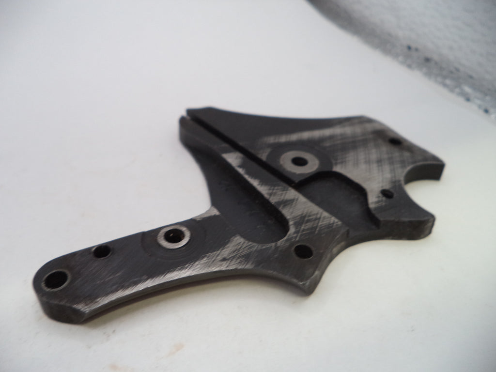 A dark gray and black brushed metal mechanical part with multiple screw holes, photographed on a white surface.
