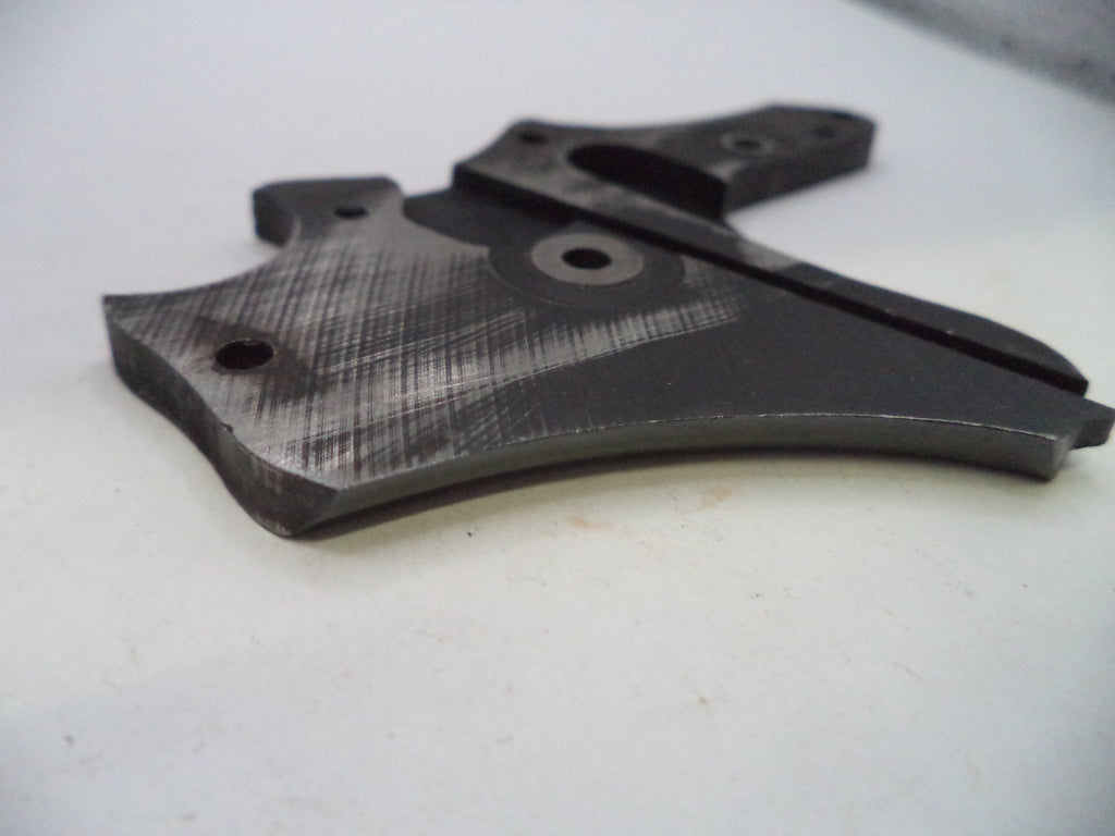 A dark gray metal replacement part with a brushed finish and a textured pattern, photographed on a light gray surface.