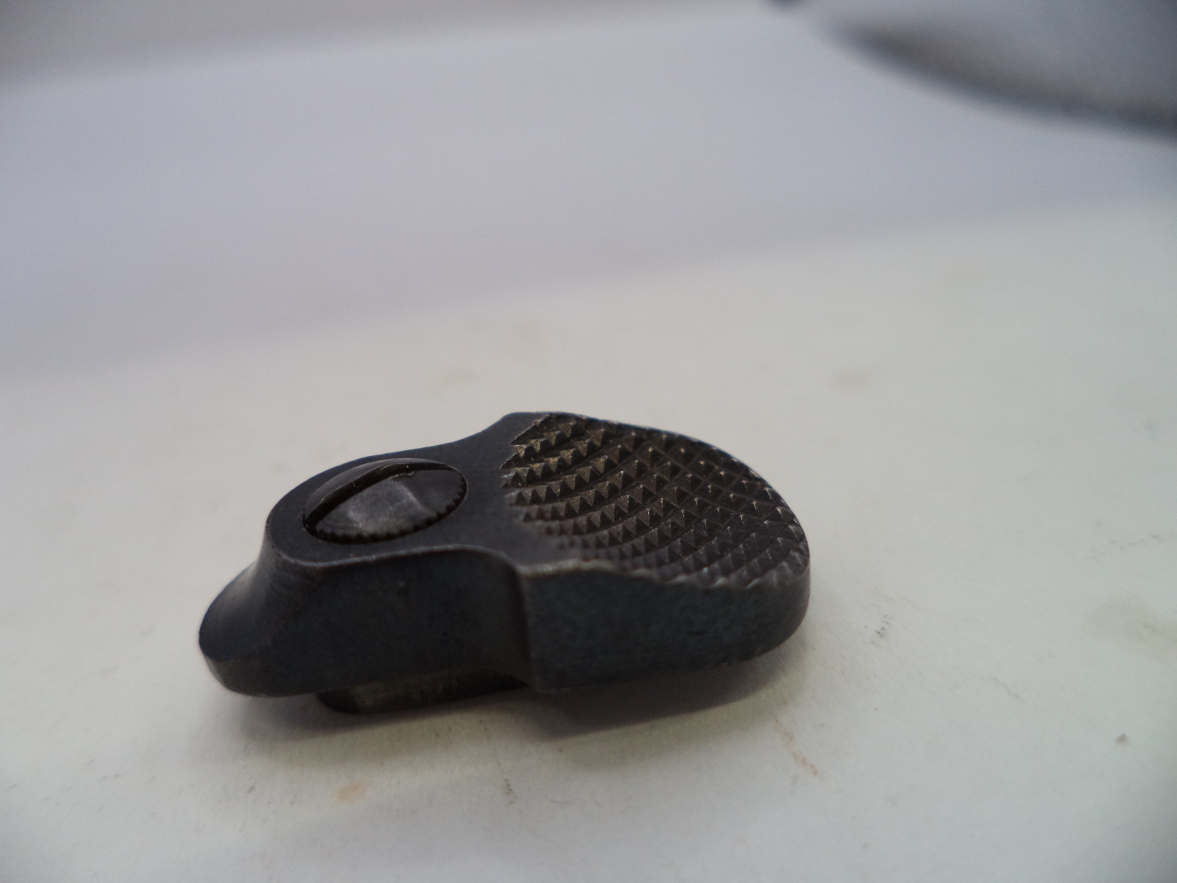 A small black textured metal hardware piece, possibly a latch or knob, resting on a light-colored surface.