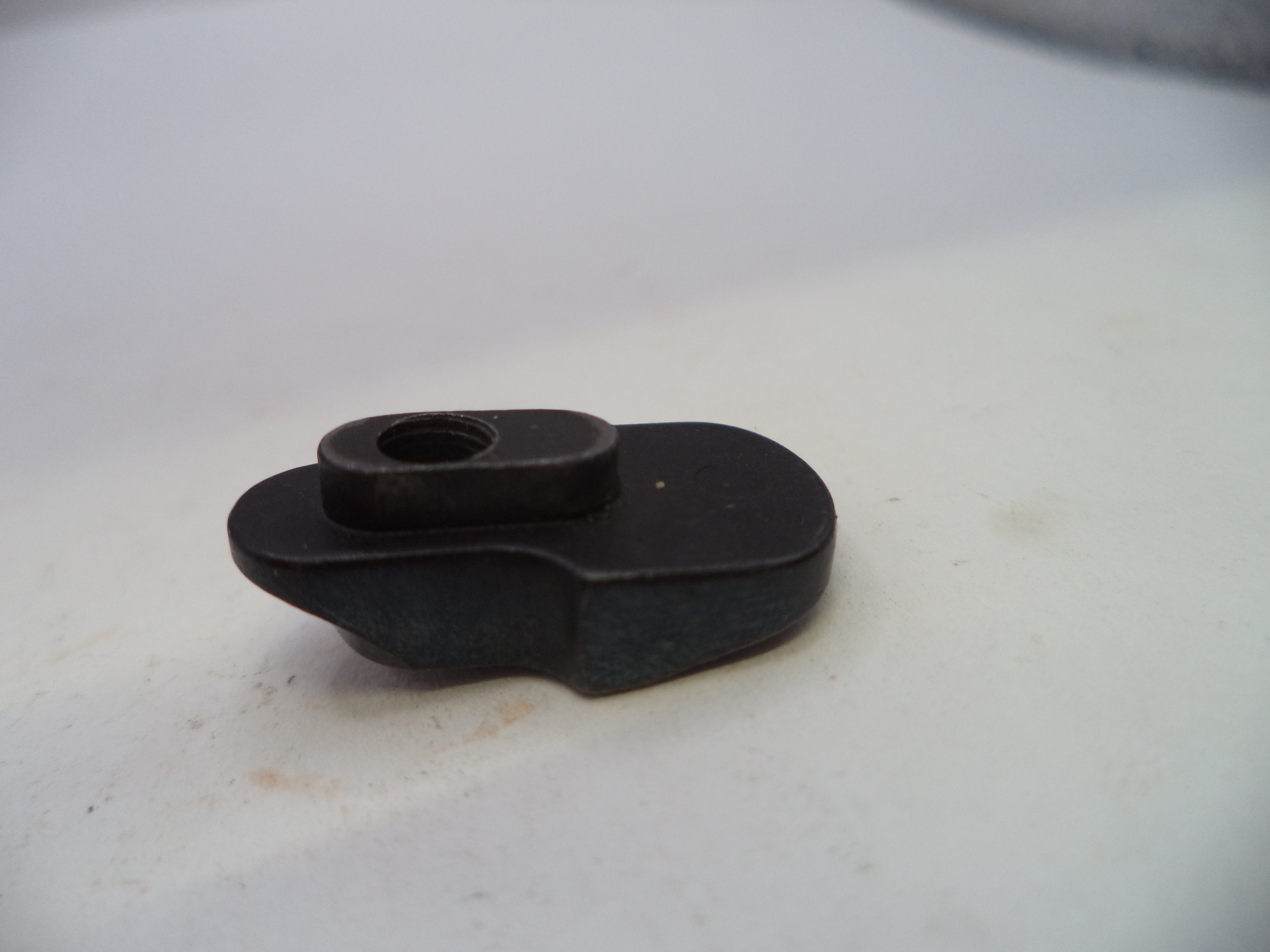A small black plastic or metal hardware component with a circular opening, photographed on a plain off-white surface.