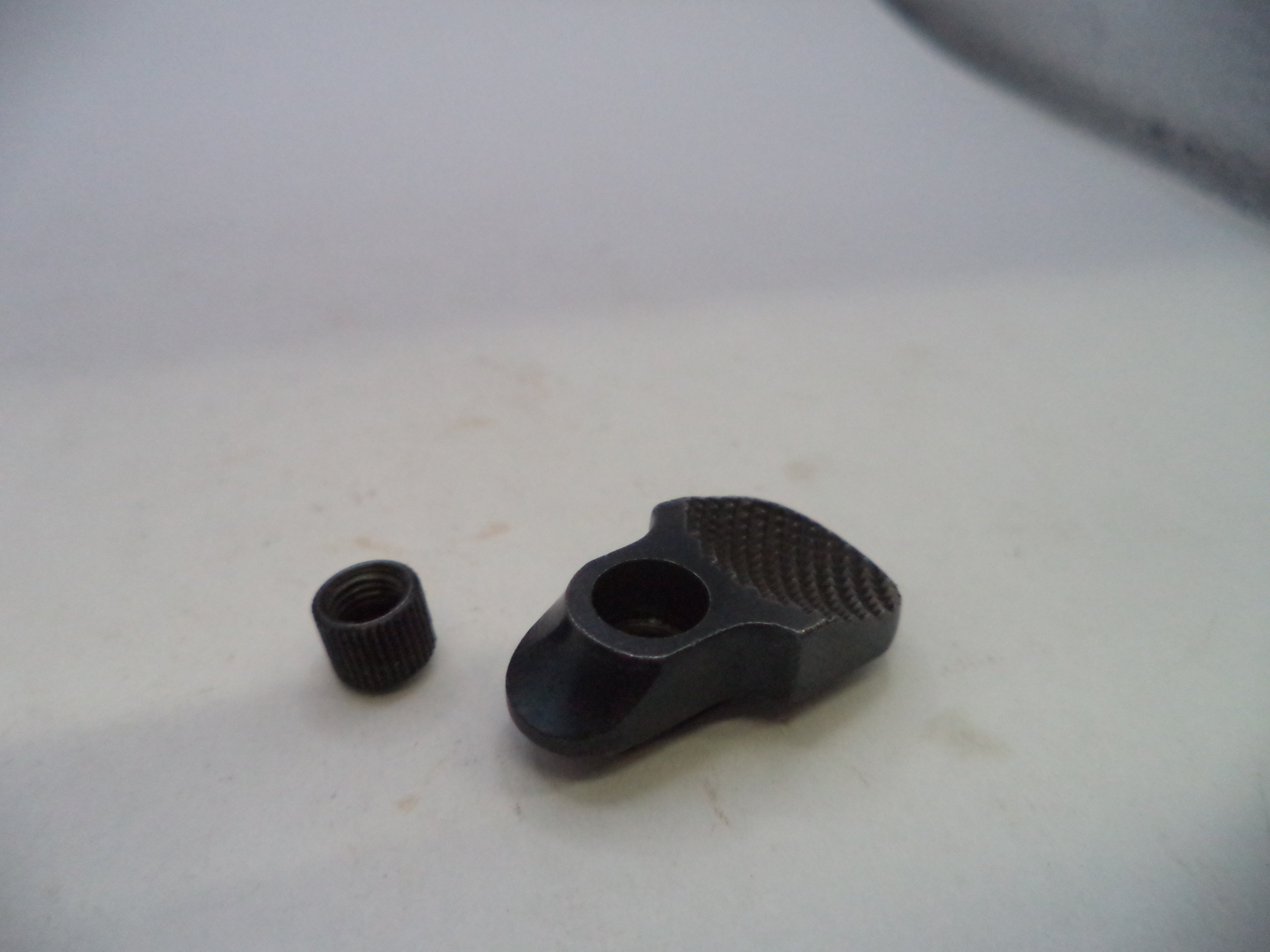 A small black metal hardware component with a textured grip surface and a separate matching threaded cap, photographed on a plain off-white surface.