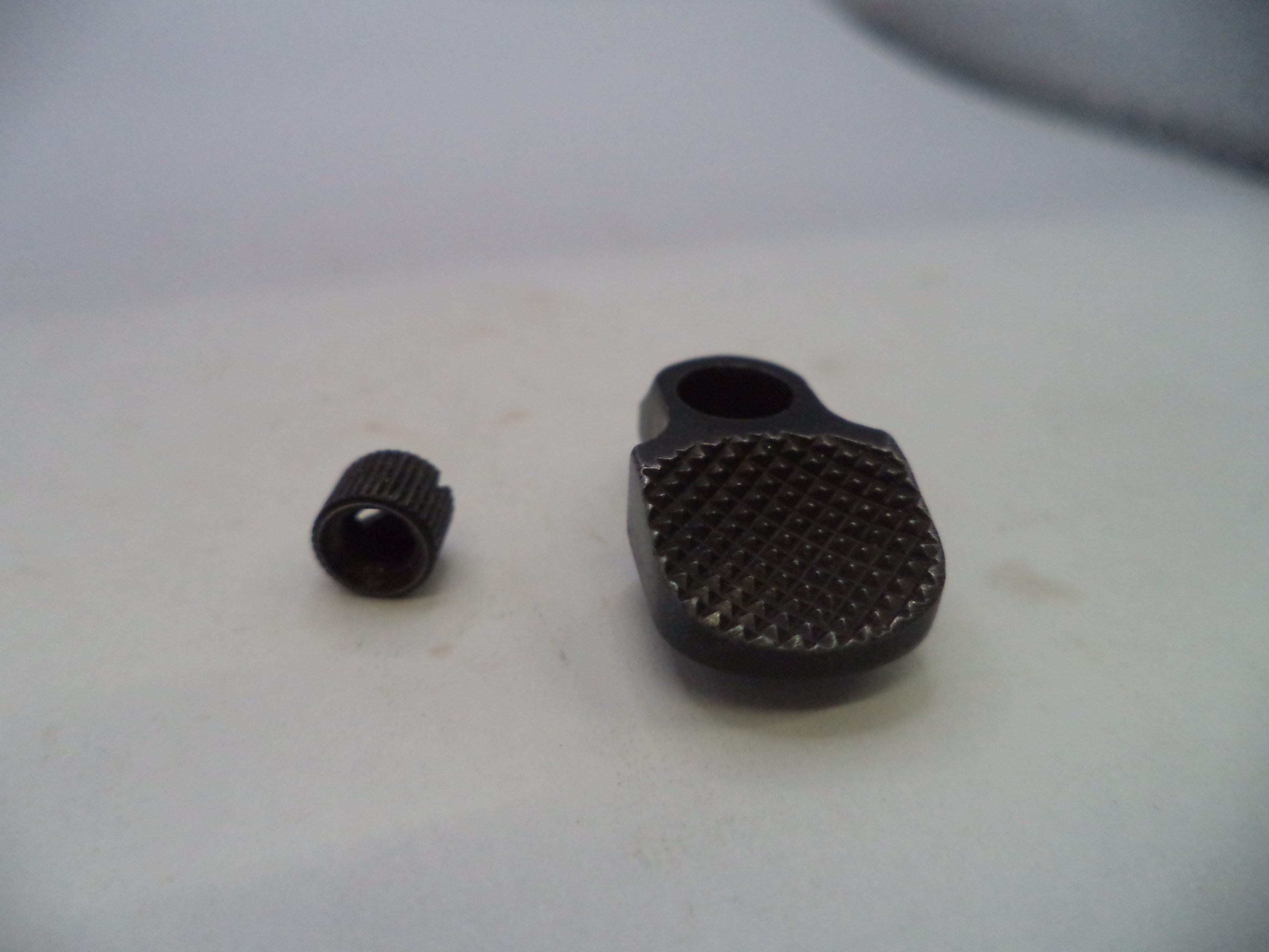 A close-up of a small black textured metal component and a separate matching cap on a light gray surface.