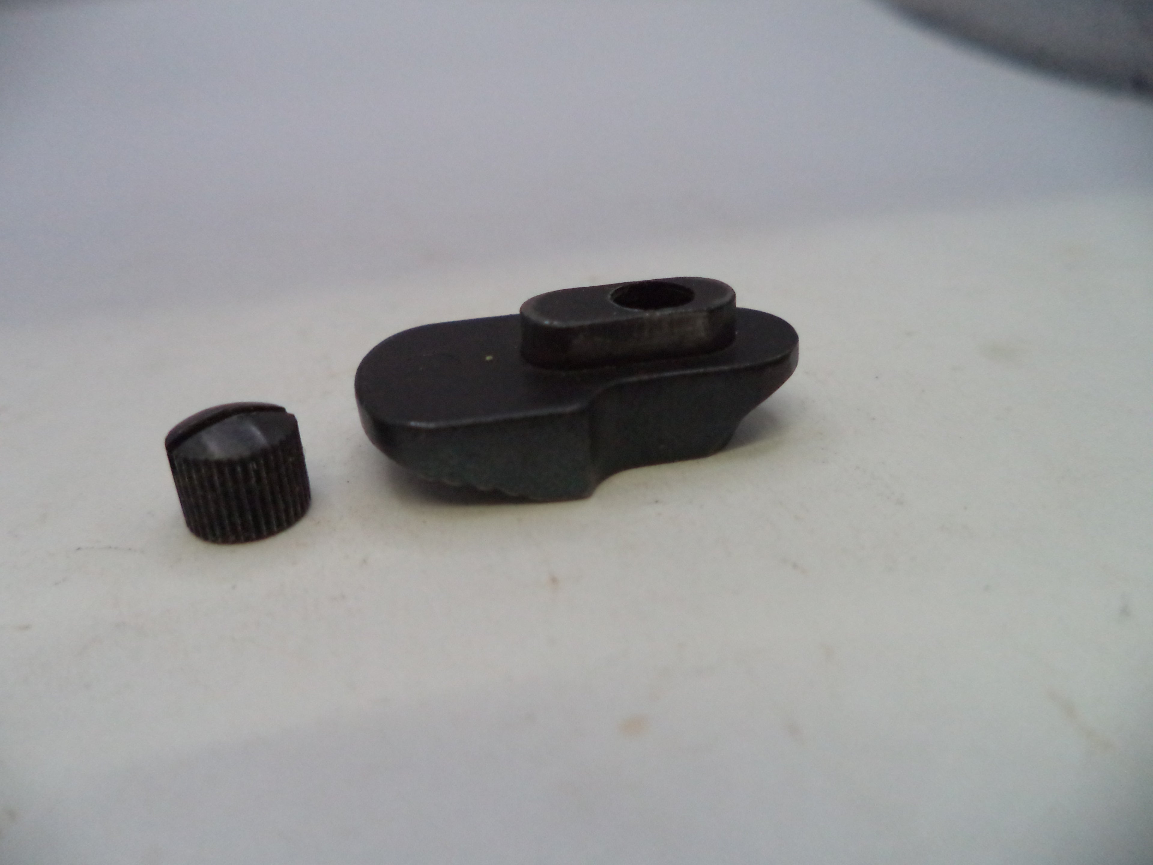 A small black plastic or metal object with a ribbed cylindrical cap-like piece beside it, photographed on a plain light background.