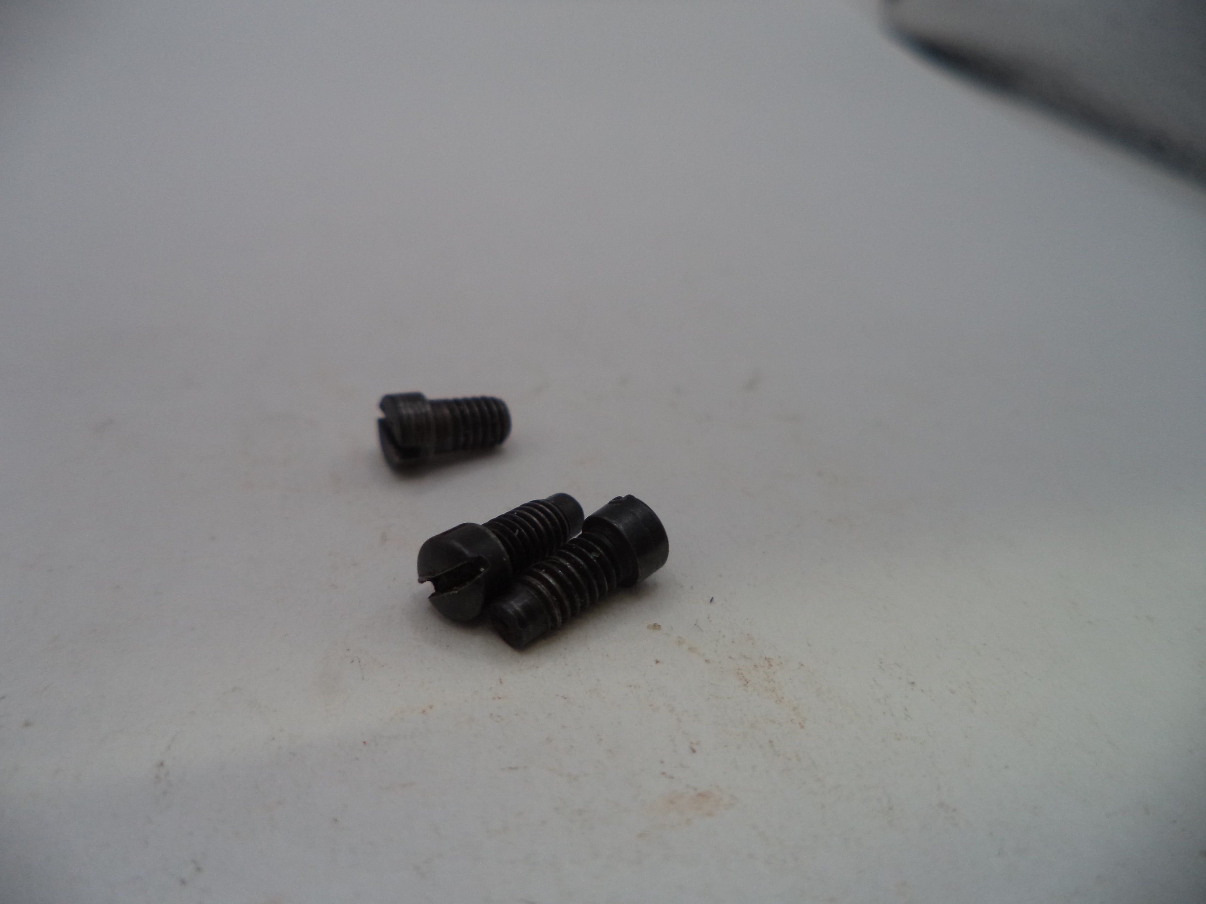 Three small black metal screws with threaded shafts and slotted heads, resting on a light gray surface.