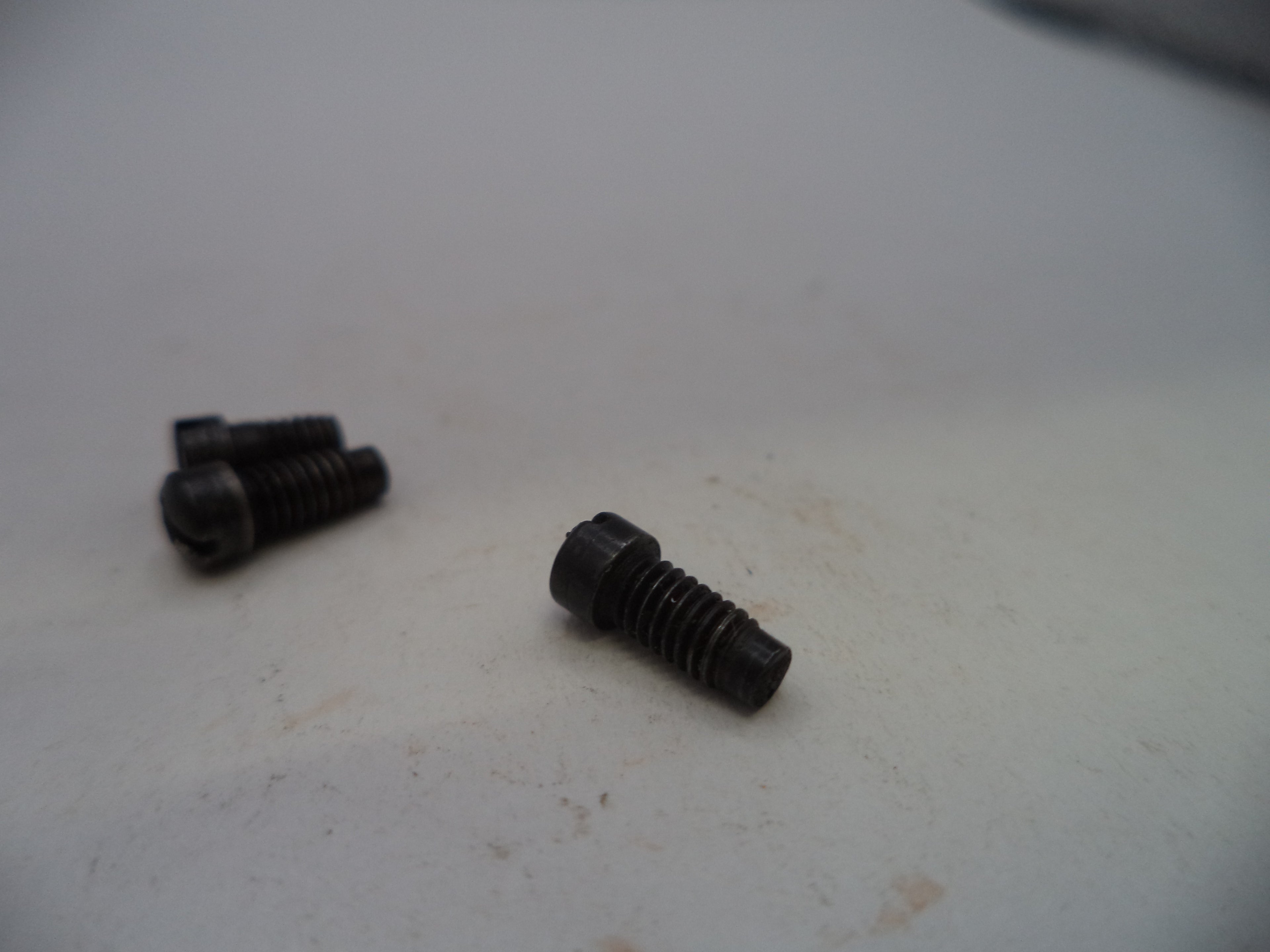 Three small black metal screws with threaded shafts and flat heads, placed on a light off-white surface.
