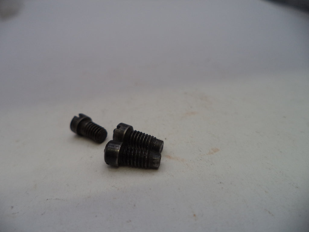 Two small dark metal threaded screws or bolts placed on a plain off-white surface.