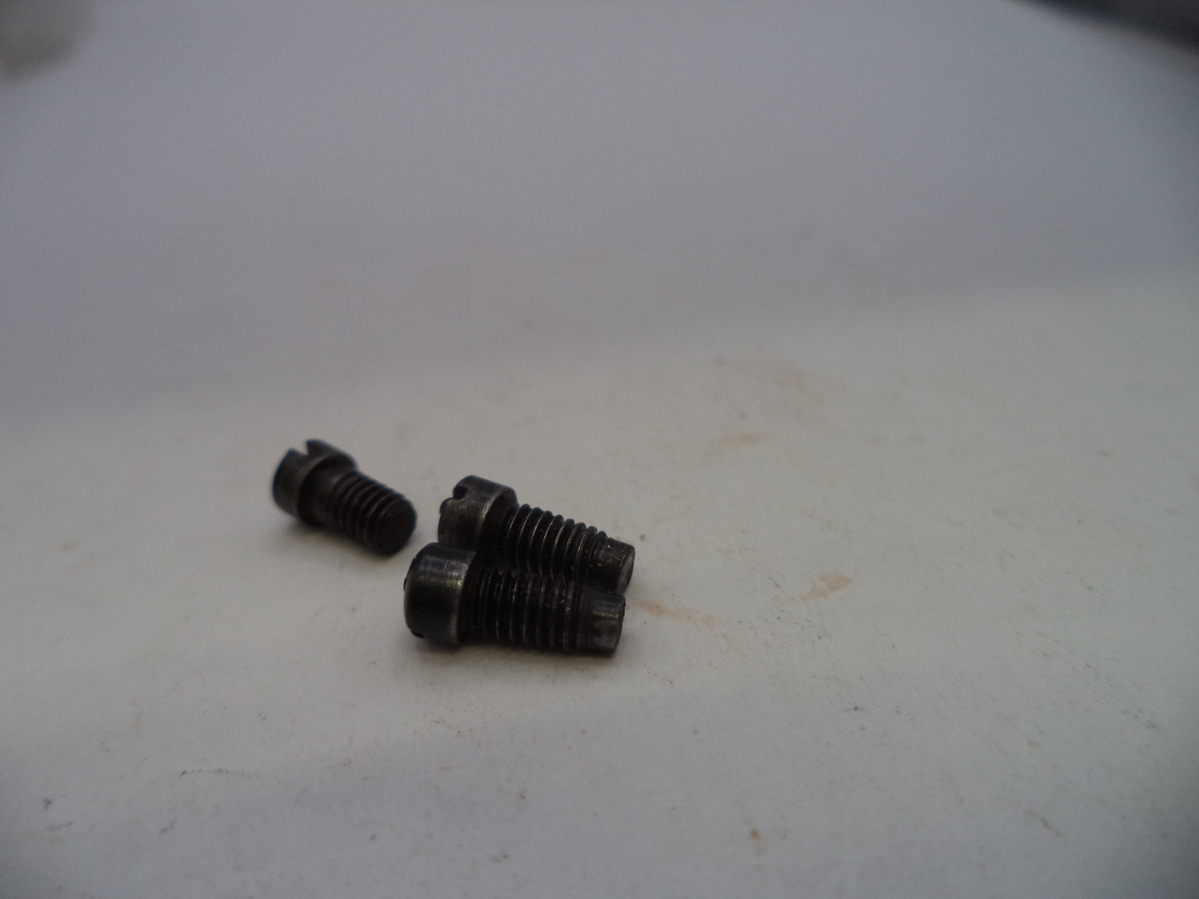 Two small dark metal threaded screws or bolts placed on a plain off-white surface.