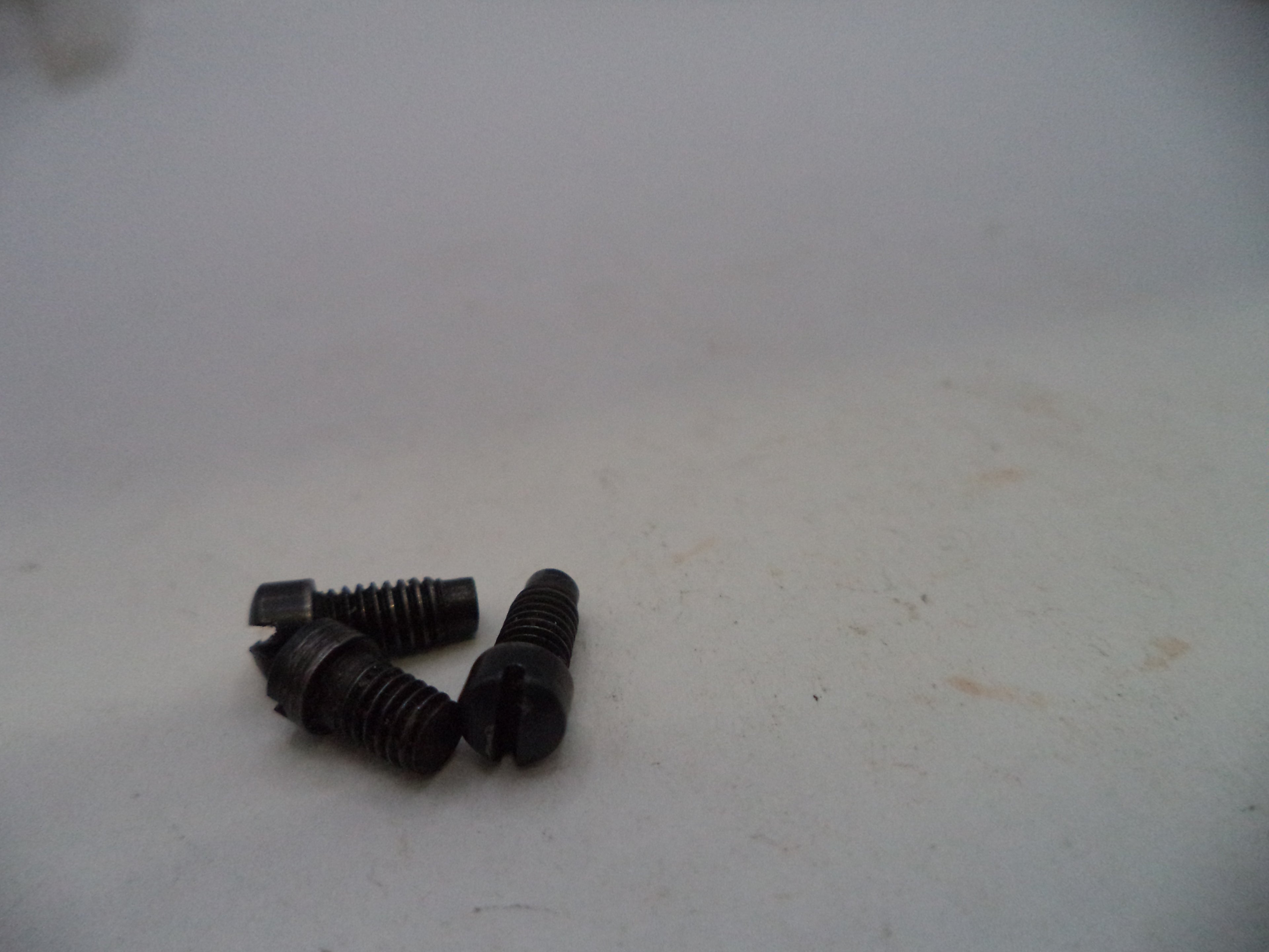 Three small black metal screws with threaded shafts and flat heads, resting on a plain off-white surface.
