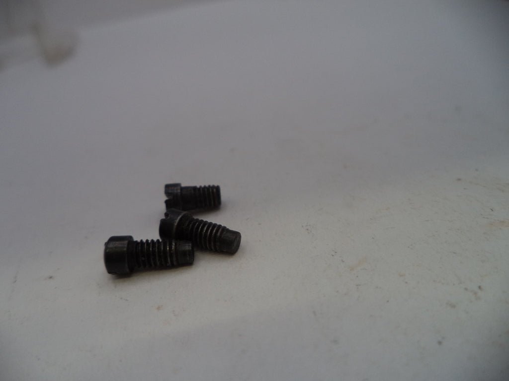 Three small black metal threaded screws on a plain off-white surface.