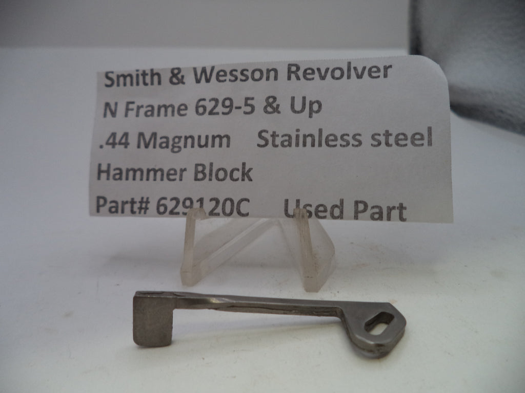 A small metal hammer block part displayed on a clear plastic stand in front of a printed label that reads 'Smith & Wesson Revolver N Frame 629-5 & Up .44 Magnum Stainless steel Hammer Block Part# 629120C Used Part'.