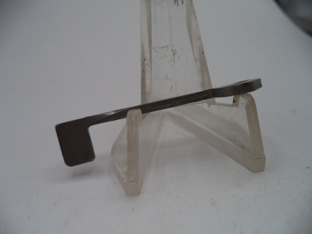 A small flat metal tool with a dark gray head and a silver curved shaft, displayed on a clear plastic stand against a white background.