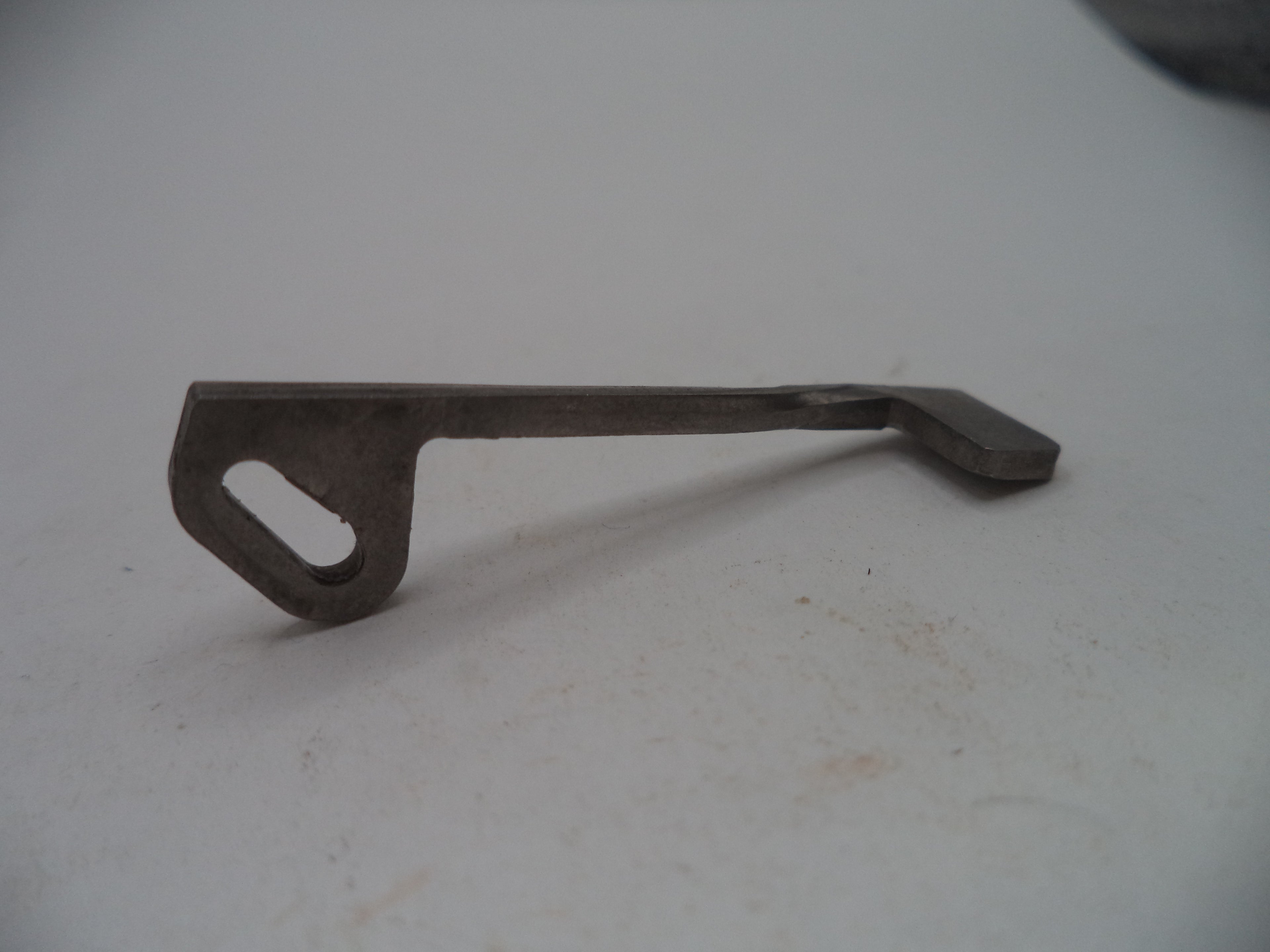 A small dark metal tool or hardware piece with a looped end and flat angled end, photographed on a plain light surface.