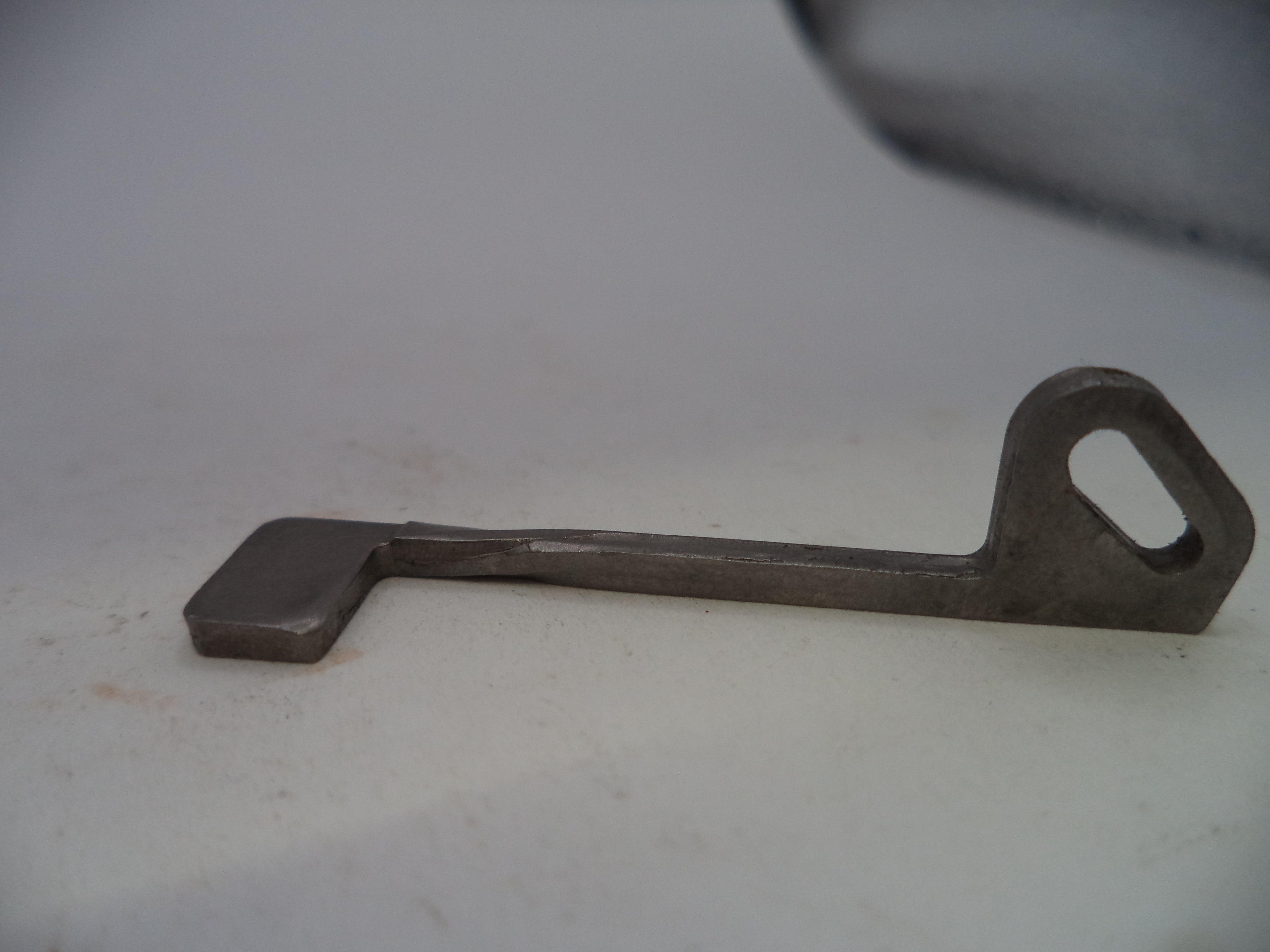 A small metal key-shaped tool with a loop at one end, photographed on a plain light background.