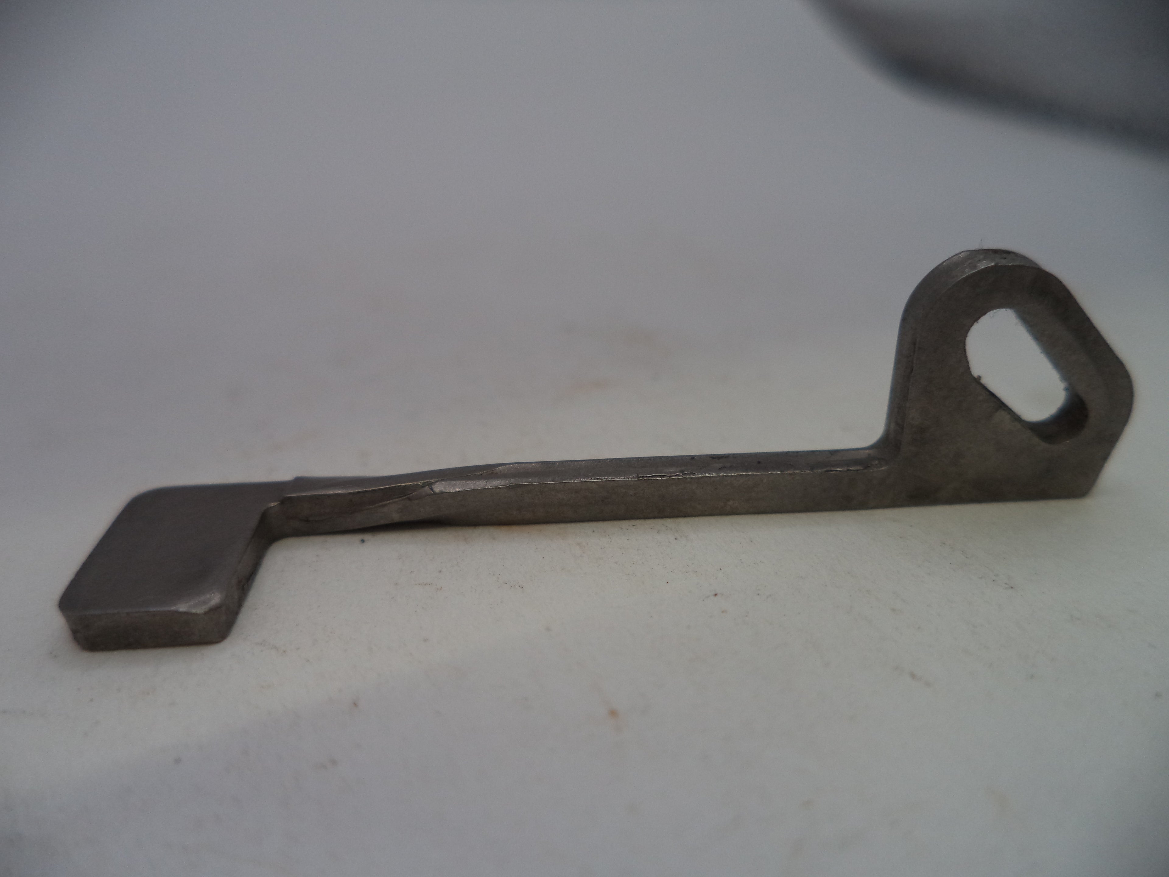 A small metal tool with a flat rectangular end and a looped handle, photographed on a plain light background.