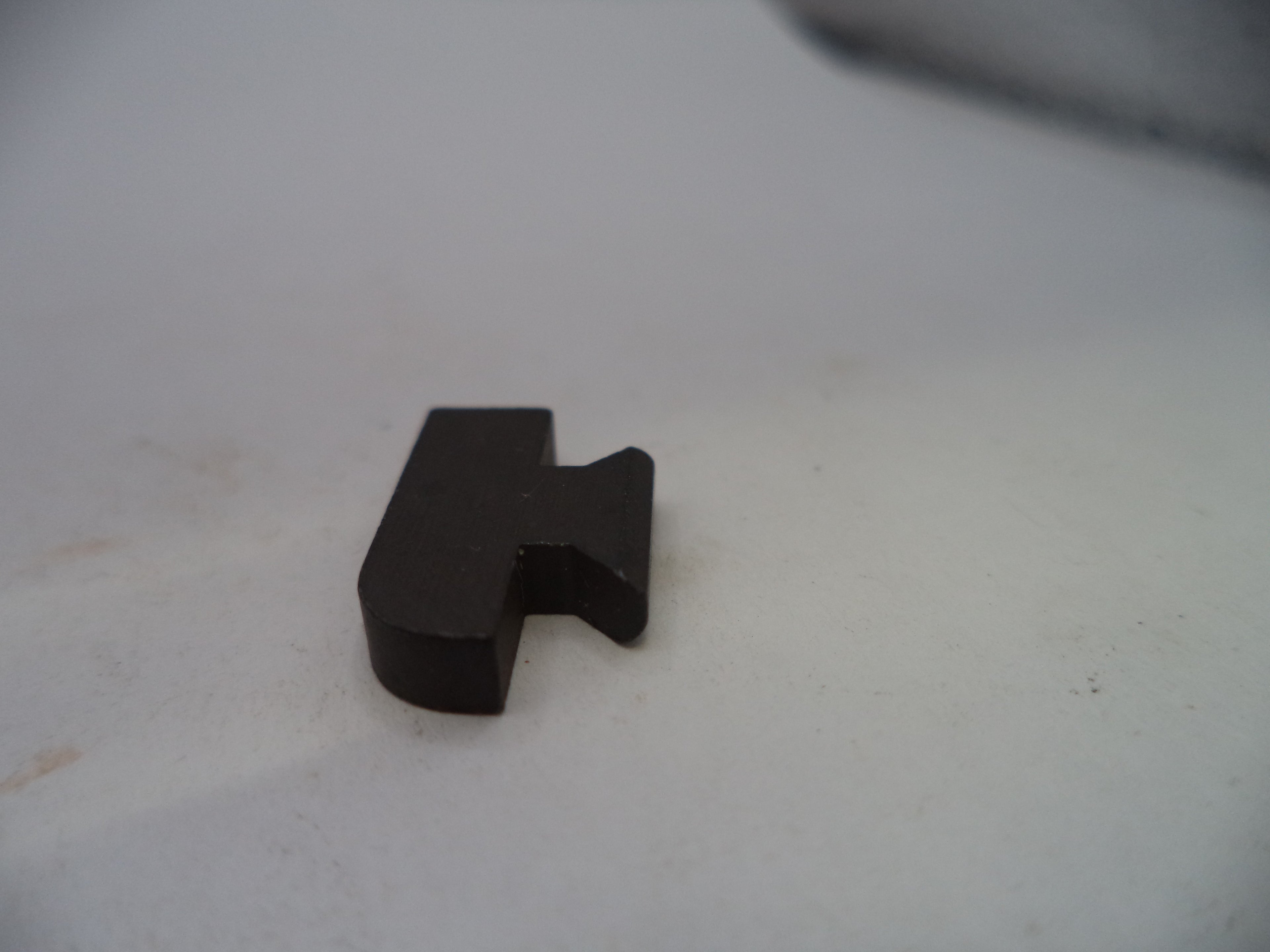 A small black plastic or metal hardware piece with a bent tab, photographed on a plain off-white surface.