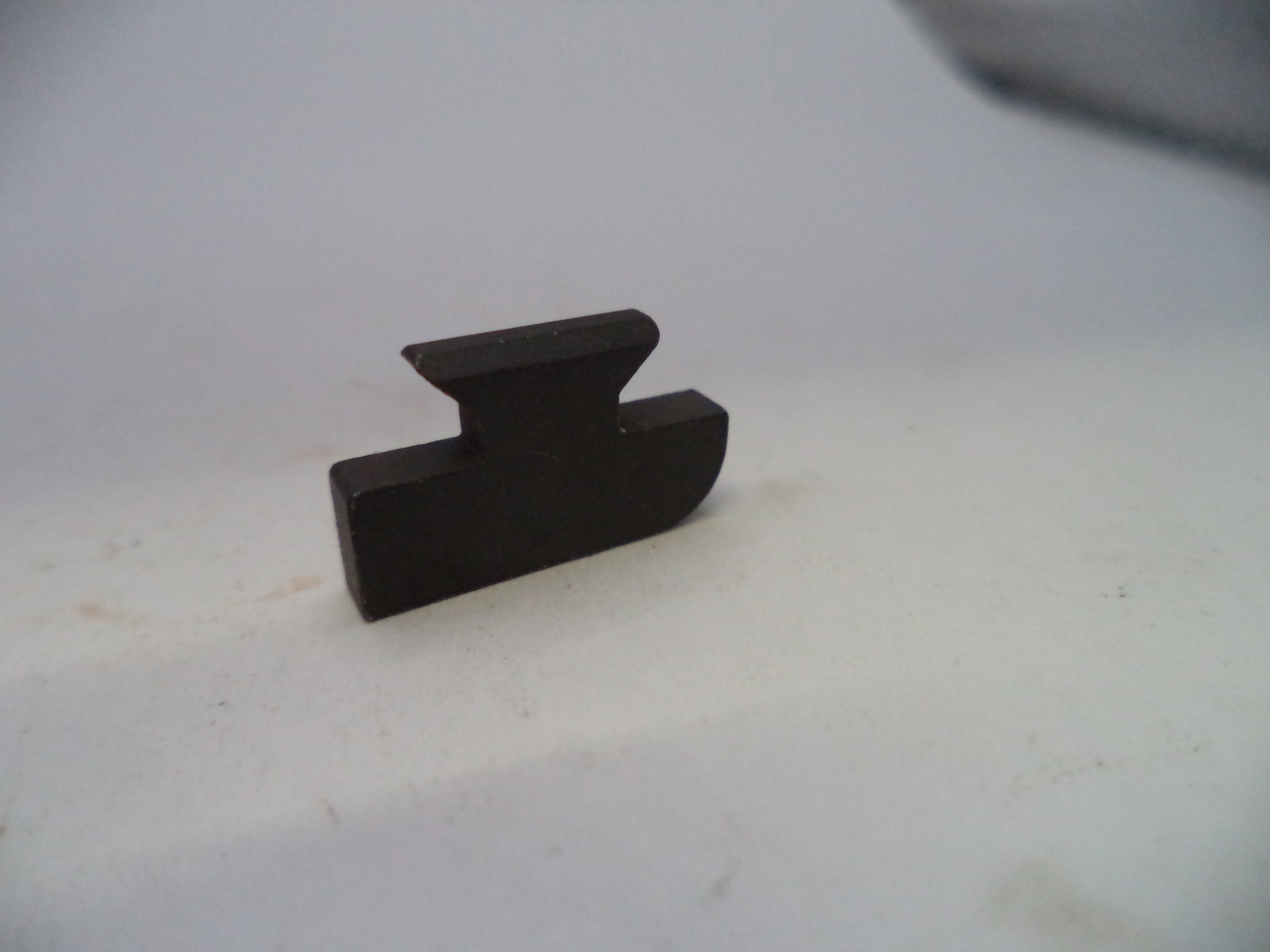 A small dark brown wooden block with a notched top, photographed on a plain off-white surface.
