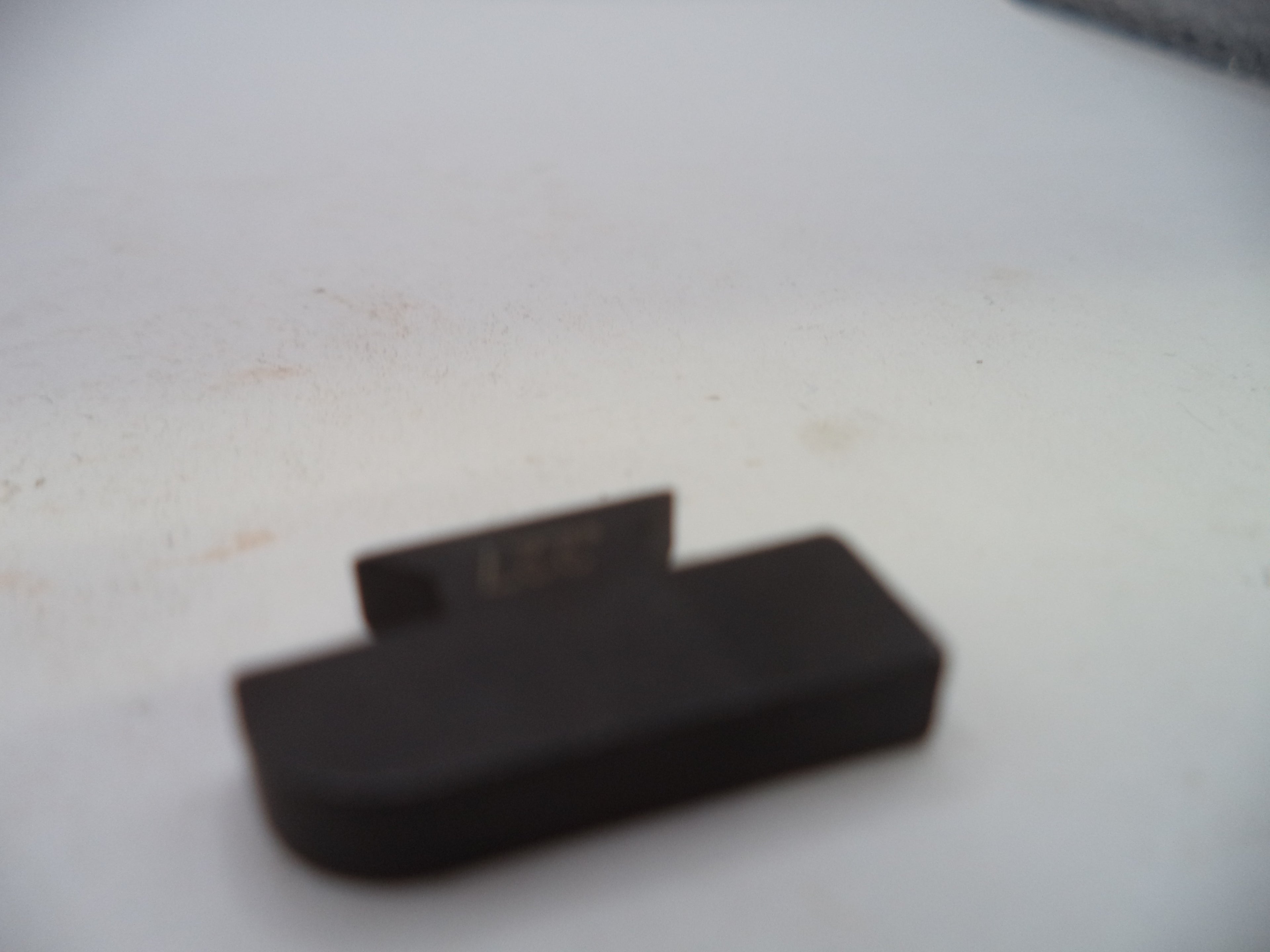 A small black plastic component with a rectangular base and a small tab, photographed on a white surface.