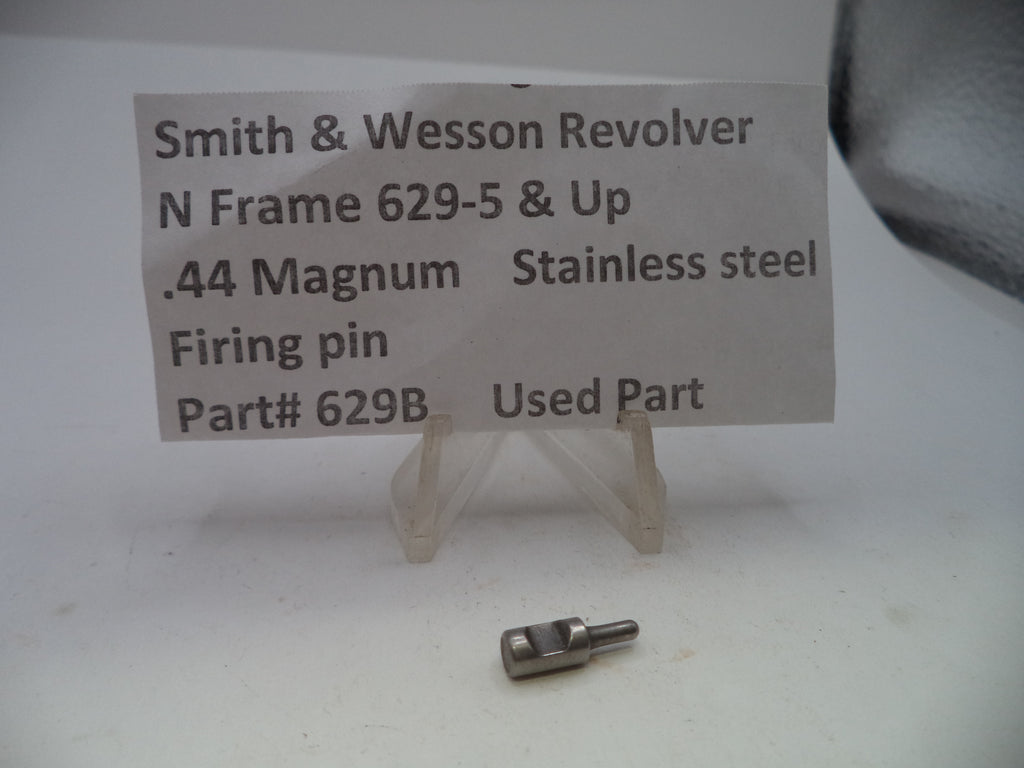 A small metallic stainless steel firing pin for a Smith & Wesson revolver, displayed on a clear plastic stand below a paper label identifying the part.