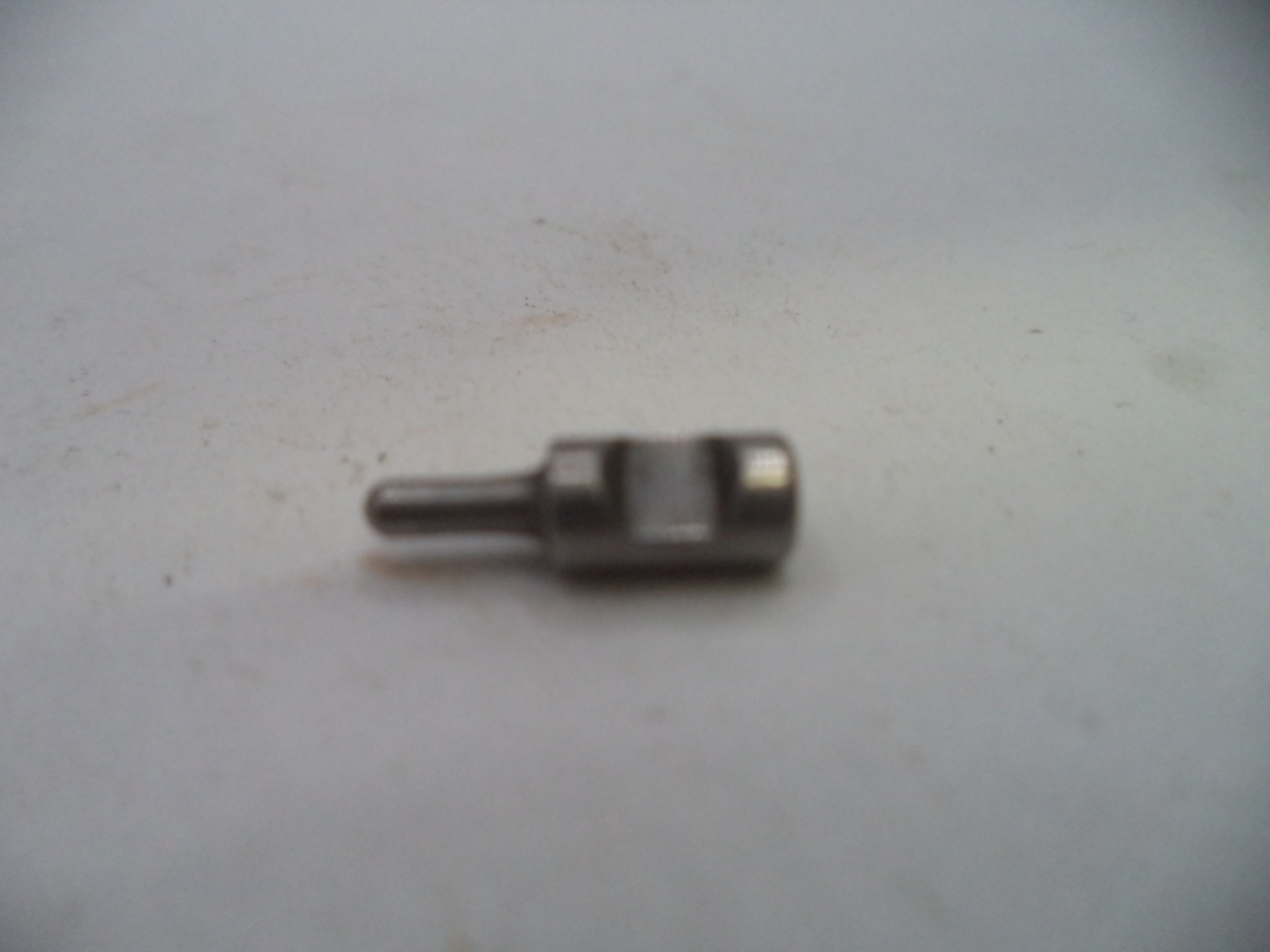 A small metallic mechanical pin or connector with a cylindrical shaft and a square-shaped head, resting on a light gray surface.