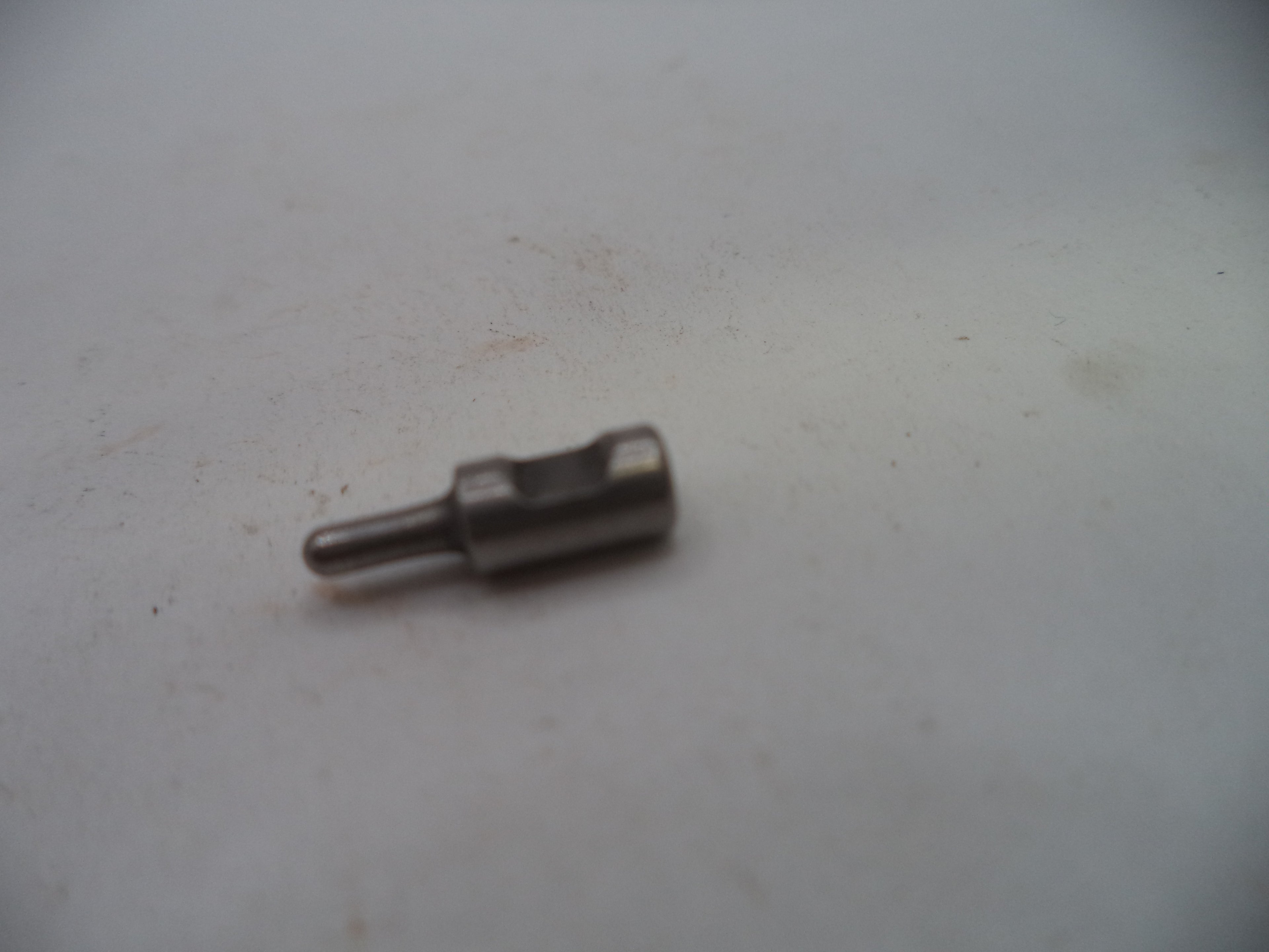 A small metallic cylindrical pin or connector with a flat head, shown on a plain off-white surface.